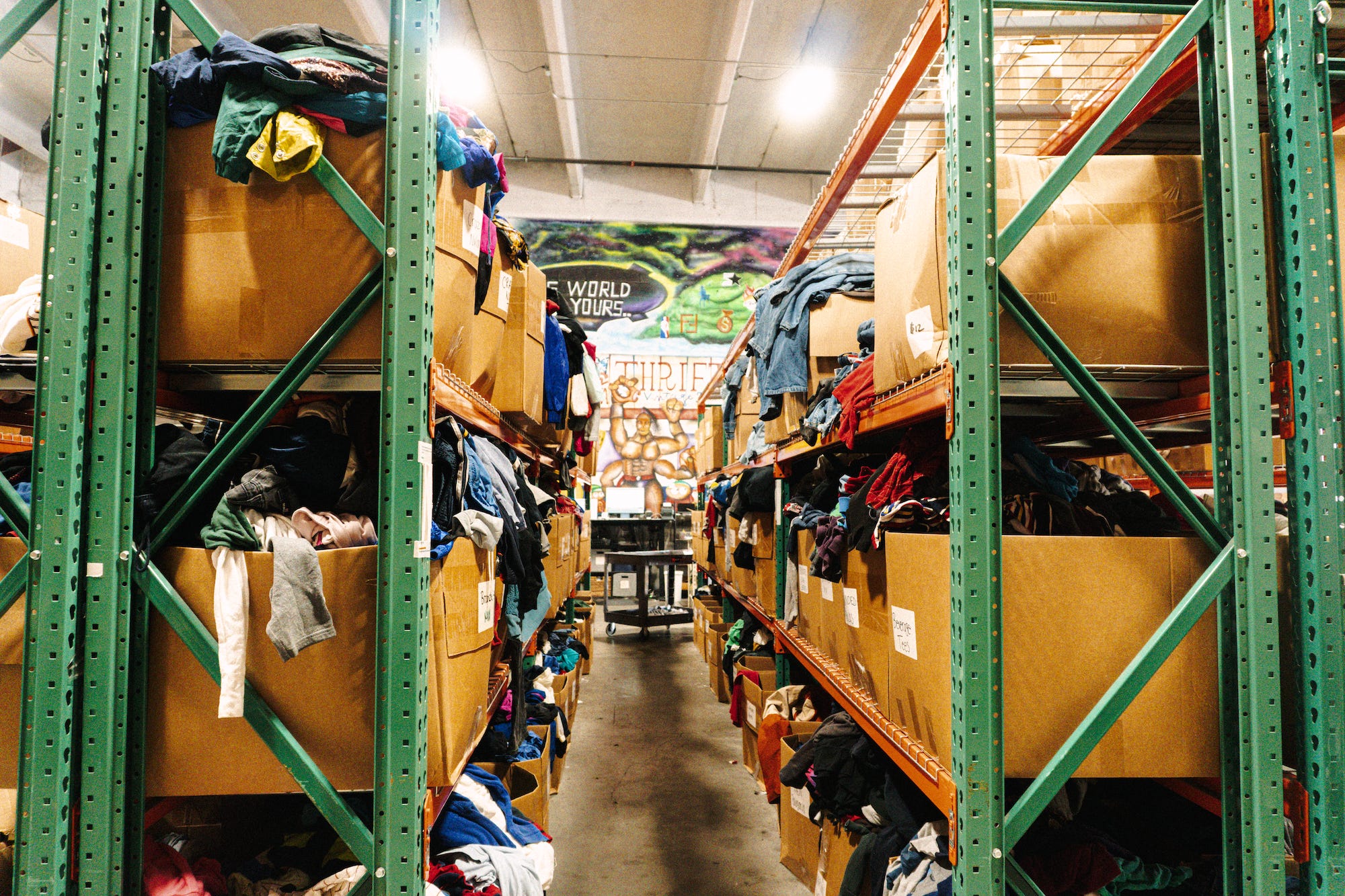 An aisle of clothing in boxes on shelves in the Thrift Vintage Fashion warehouse.