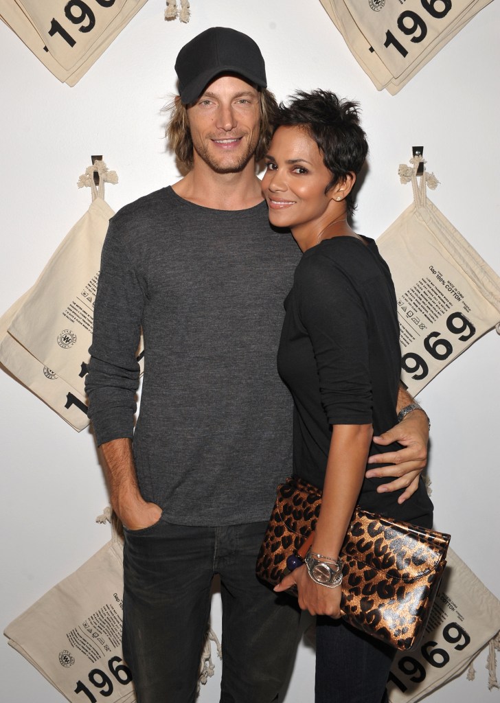 Gabriel Aubry in a grey baseball cap, grey t-shirt and grey pants.  Halle Berry in a black dress, carrying a leopard print clutch.