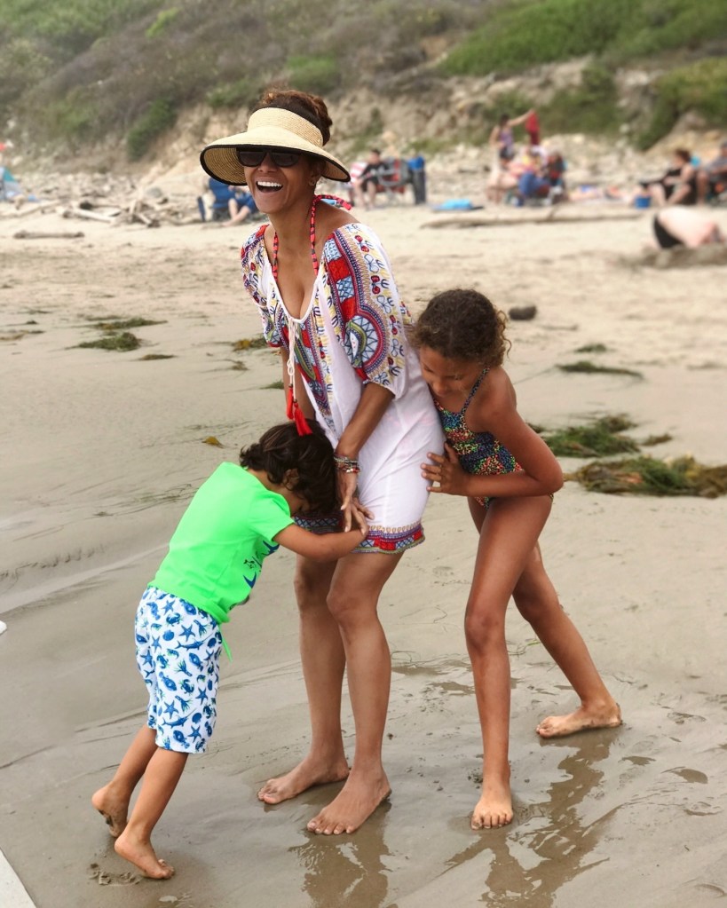 Halle Berry in a white embroidered wrap and sun visor. Nahla Aubry in a swimsuit, Maceo Martinez in a green t-shirt and blue shorts.