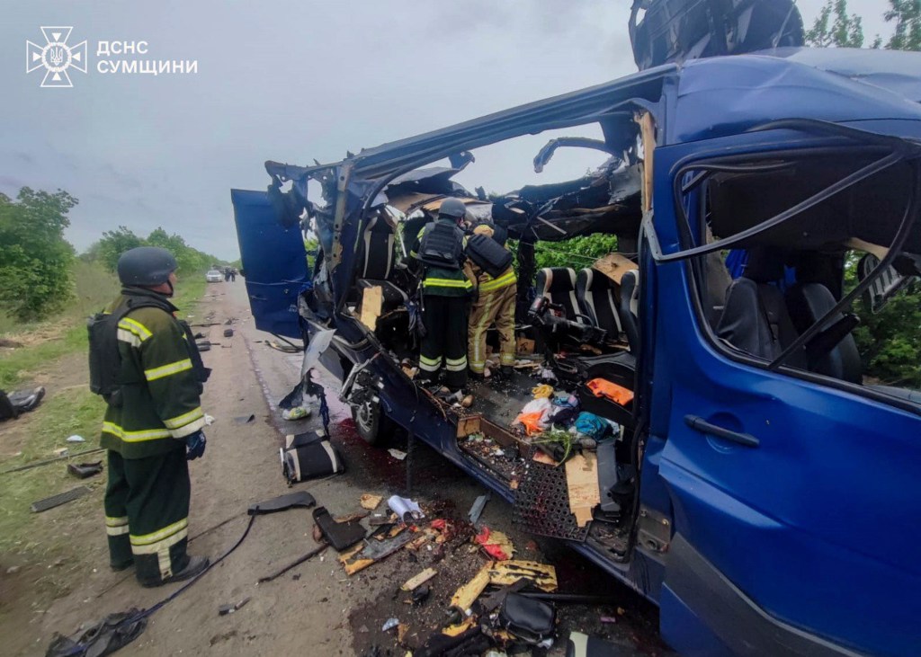 Rescuers seen working to recover the bodies of passengers after a Russian drone struck a blue passenger bus at the village of Bilopillya in the Sumy region. Debris seen scattered around destroyed bus.