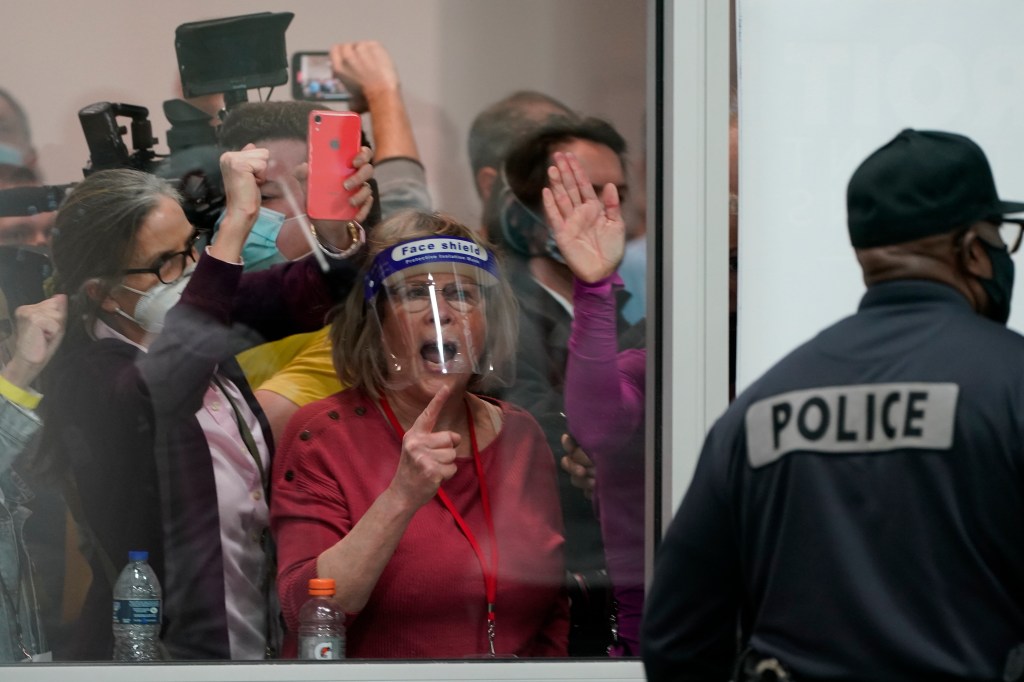Election challengers yell as they look through the windows of the central counting board as police were helping to keep additional challengers from entering due to overcrowding, Nov. 4, 2020, in Detroit.