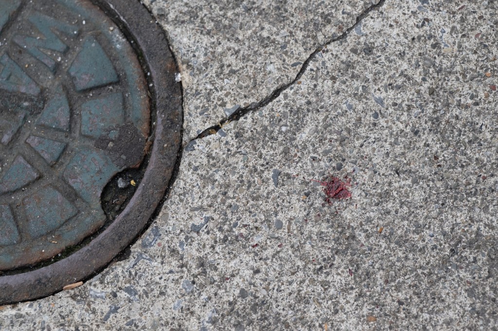 The sidewalk is stained with a small red patch where the stabbing happened.