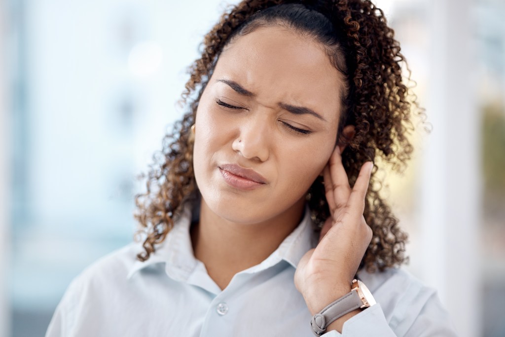 Woman suffering from ear ache due to tinnitus, indicative of potential hearing loss and nerve infection risk, seen holding ear and grimacing in pain.