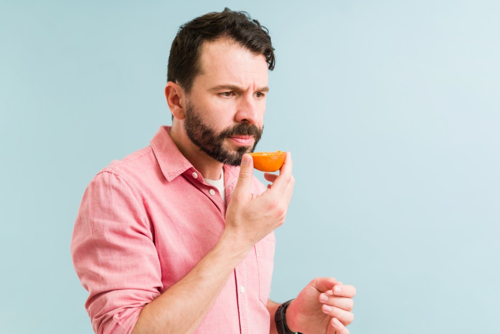 Man suffering from anosmia, holding an orange fruit in front of his nose, unable to smell