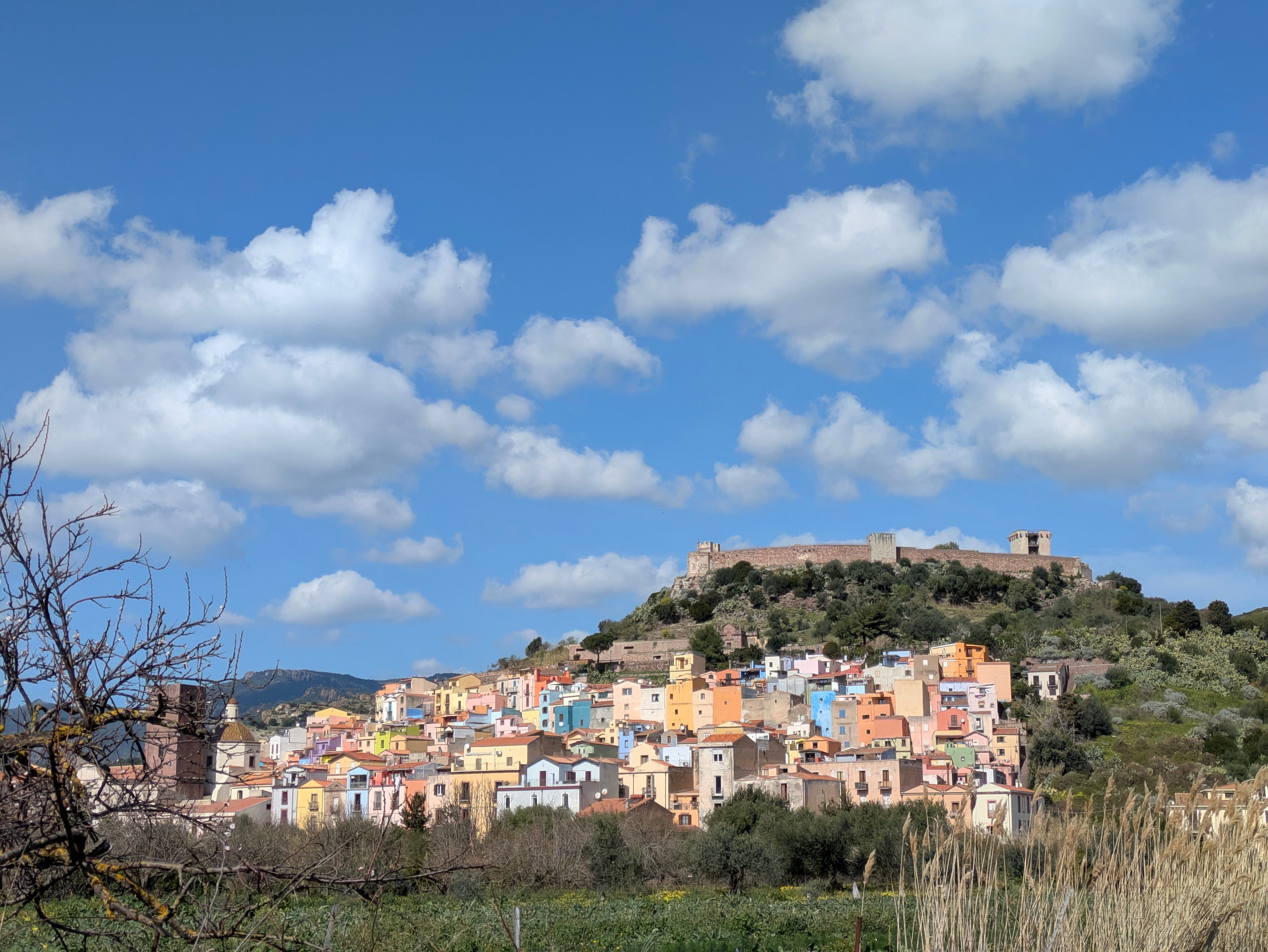 Colorful houses on a hill in Bosa, Italy, with clouds in a blue sky.