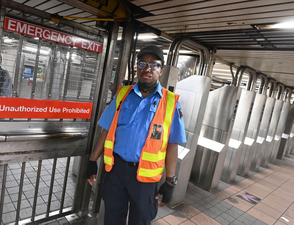 Allied Guard Romuald Zampou,52, in a blue shirt black pants and yellow and orange vest stands near the emergency gate mans the emergency exit at the West 34th St./6th Ave. subway station. 