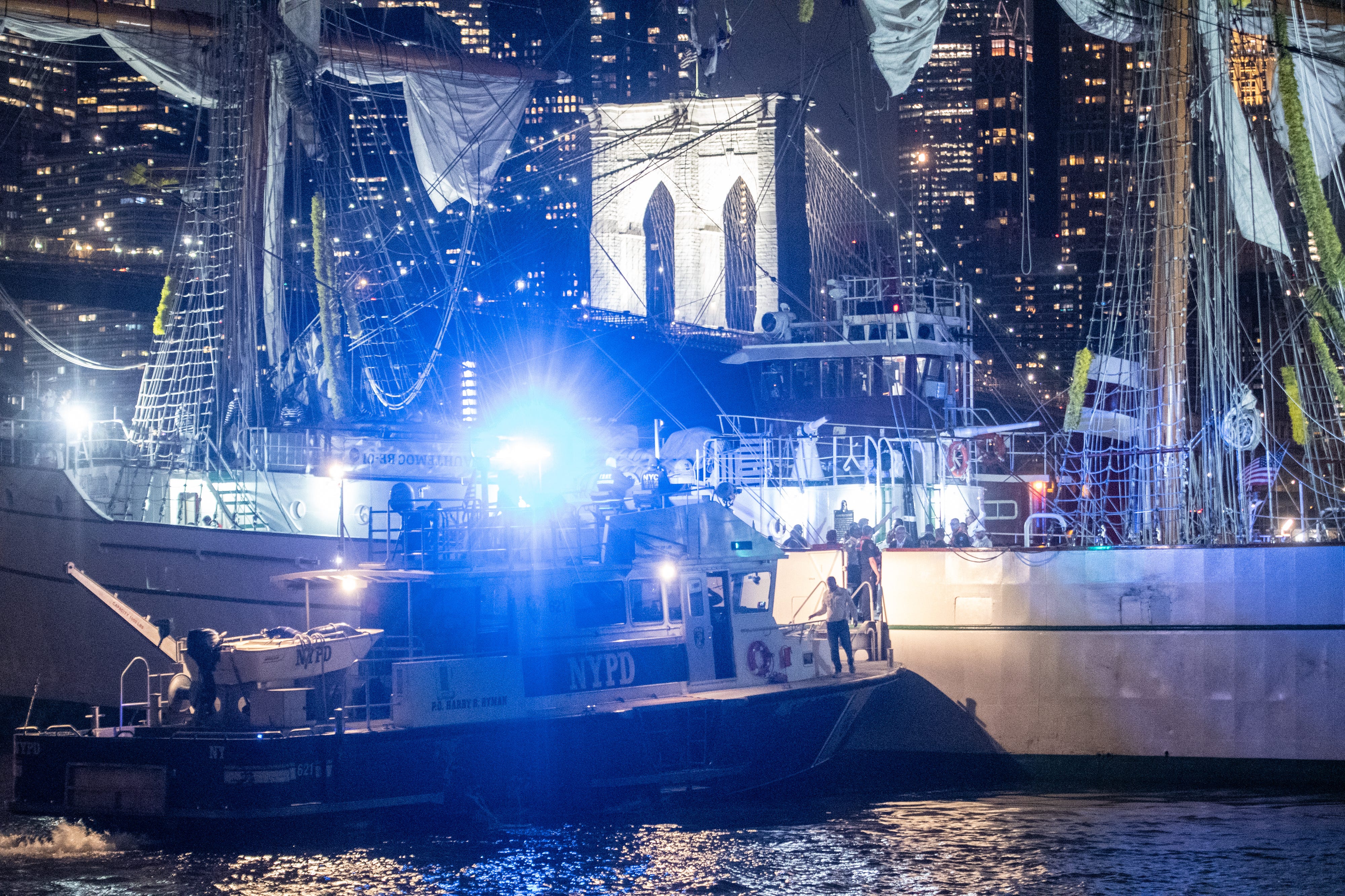 A police tugboat alongside a stricken mast sailing ship with Brooklyn bridge in the background