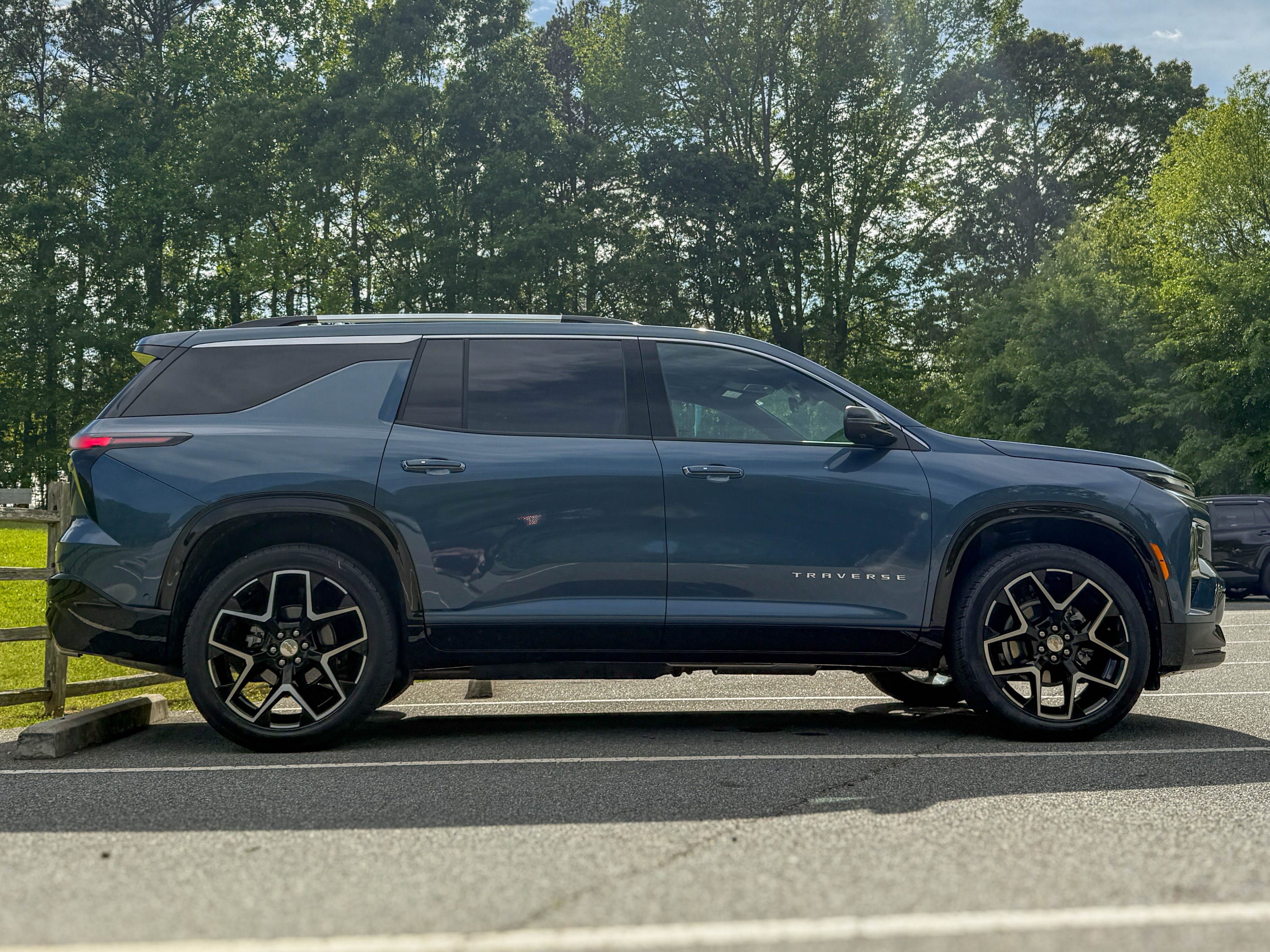 The right side of a blue 2025 Chevrolet Traverse High Country midsize family SUV parked by a field.