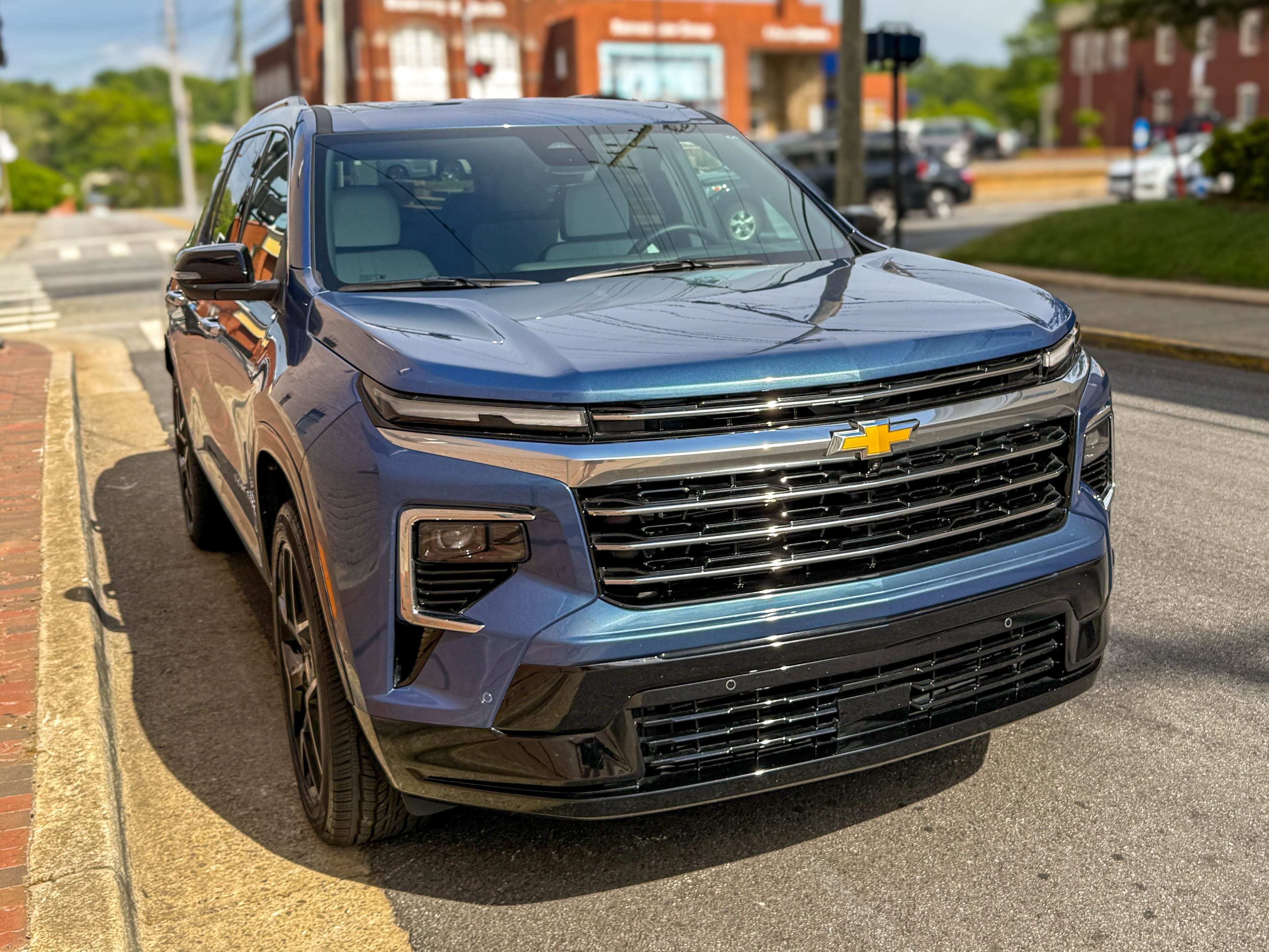 The right front corner of a blue 2025 Chevrolet Traverse High Country midsize family SUV parked on the street.