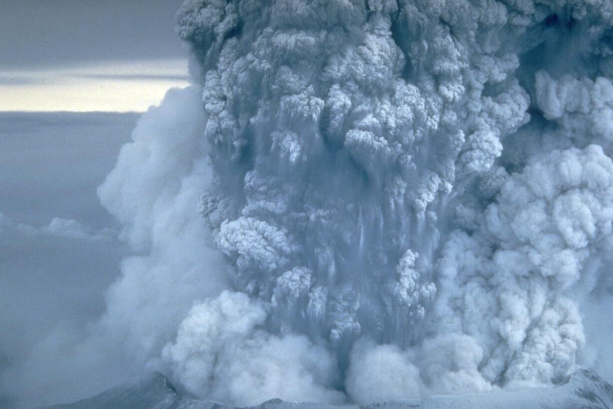 A plume of gray-white ash pouring upward from a volcano