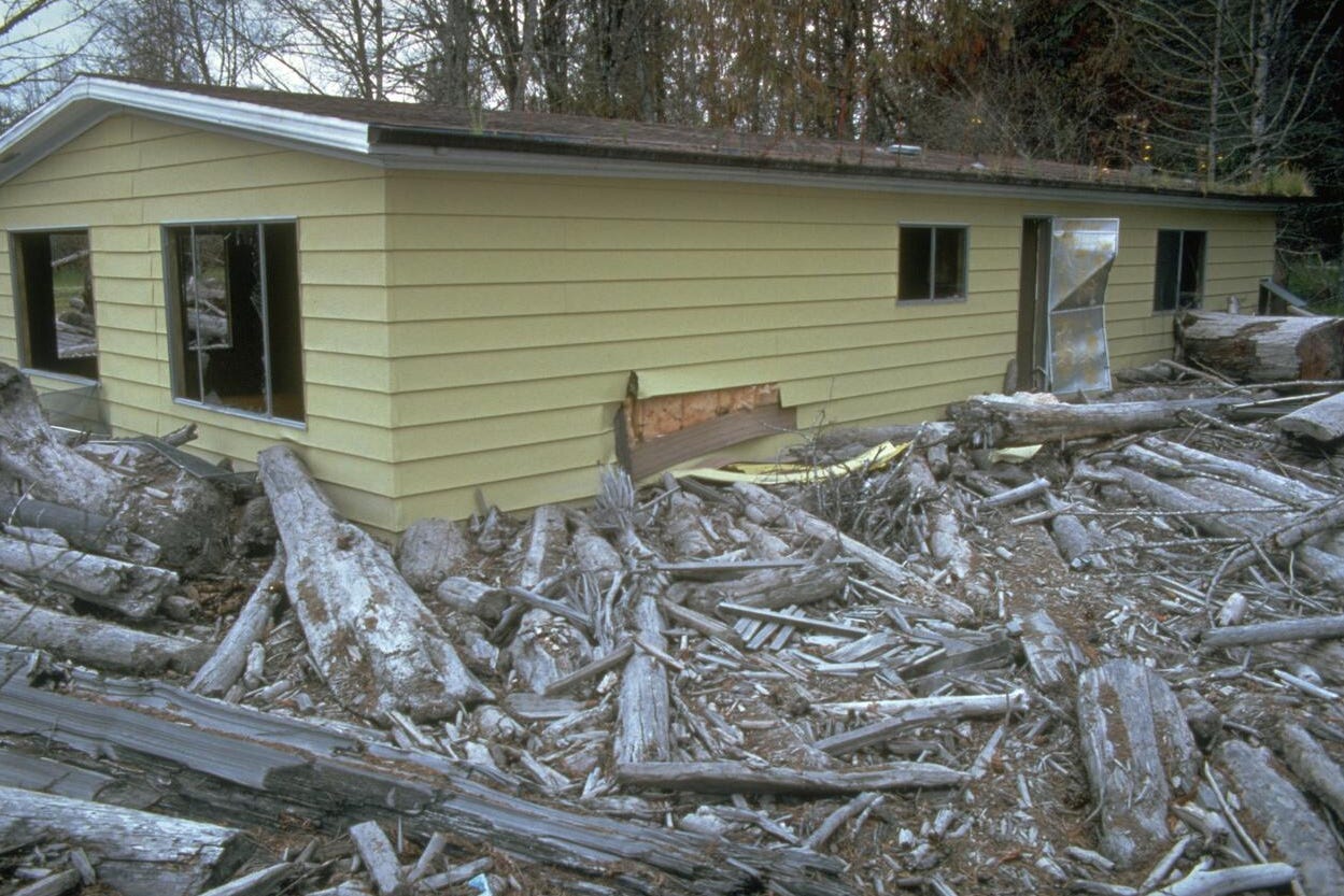 A yellow house is buried by broken trees and dirt