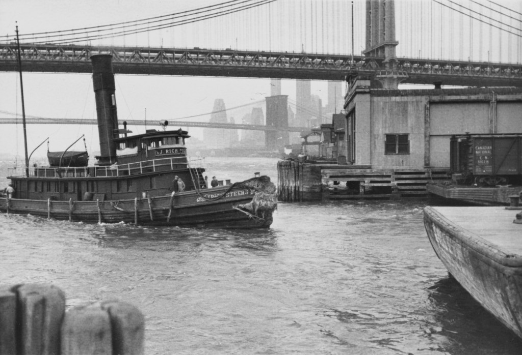A tugboat by J Rich Steers, Inc approaching Brooklyn pier under the Brooklyn Bridge over the East River, circa 1935.