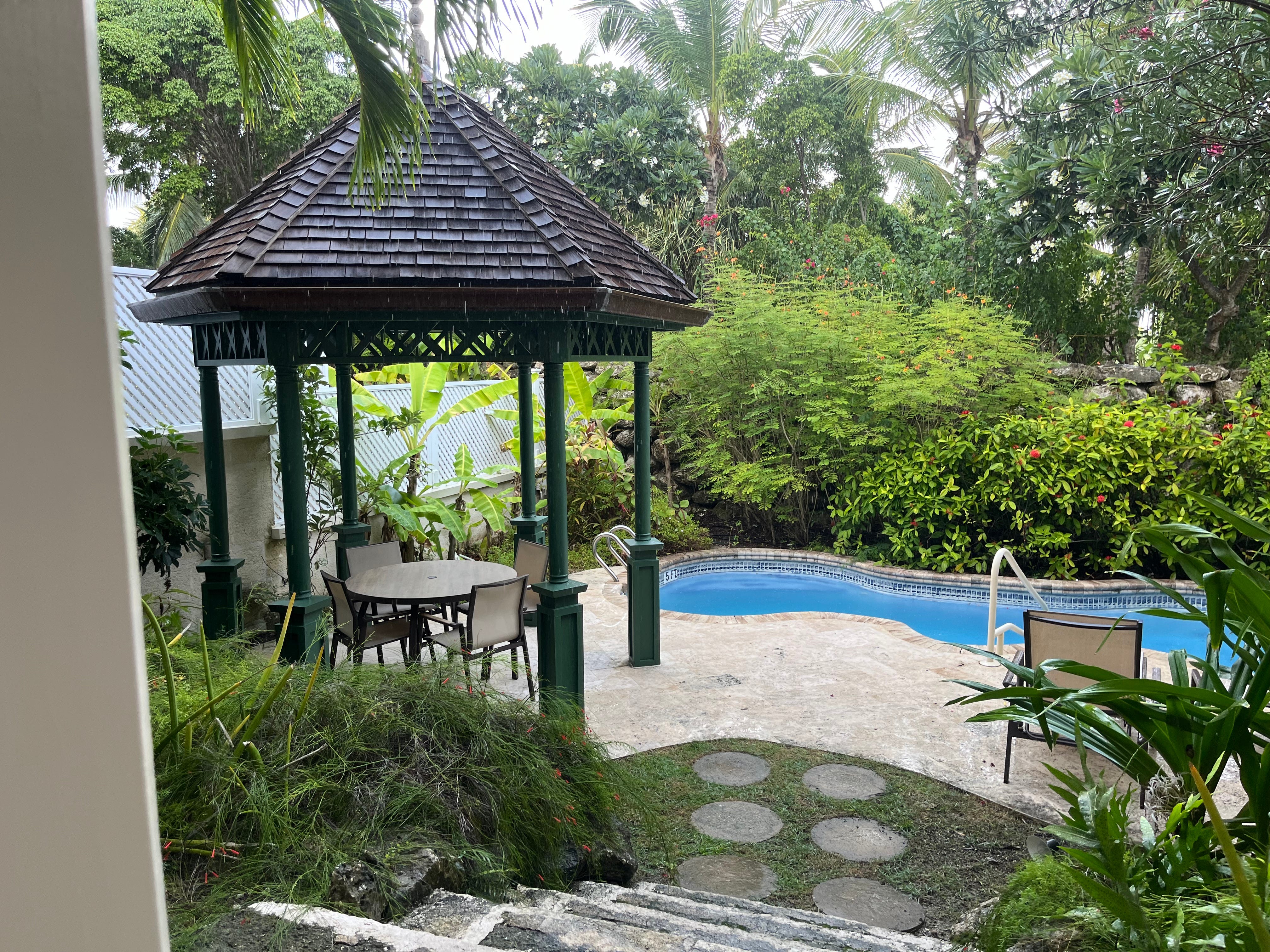 A private area with a pool and a covered dining area with tables and chairs that's surrounded by greenery and trees.