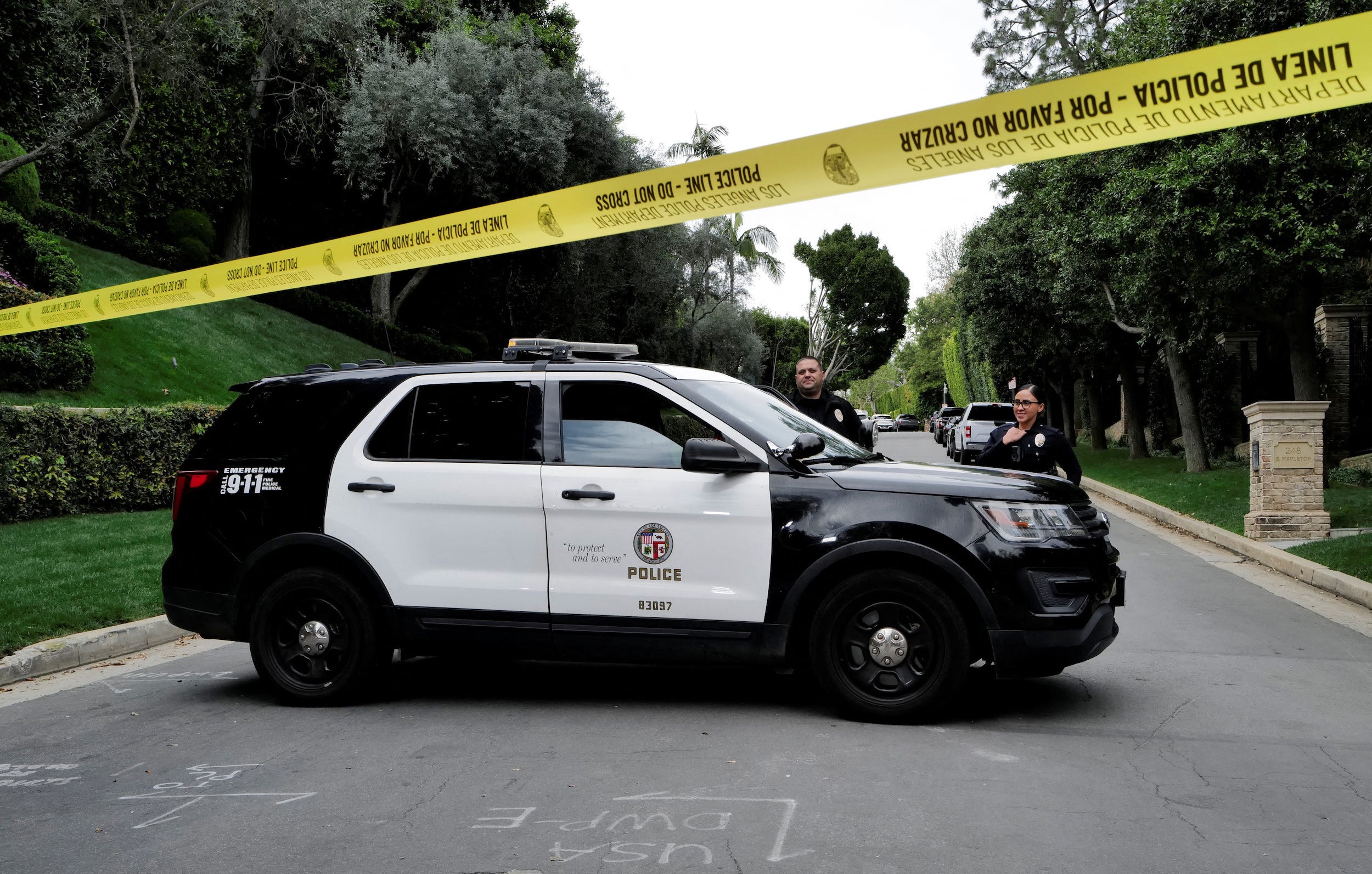 Law enforcement officers stand behind police tape.