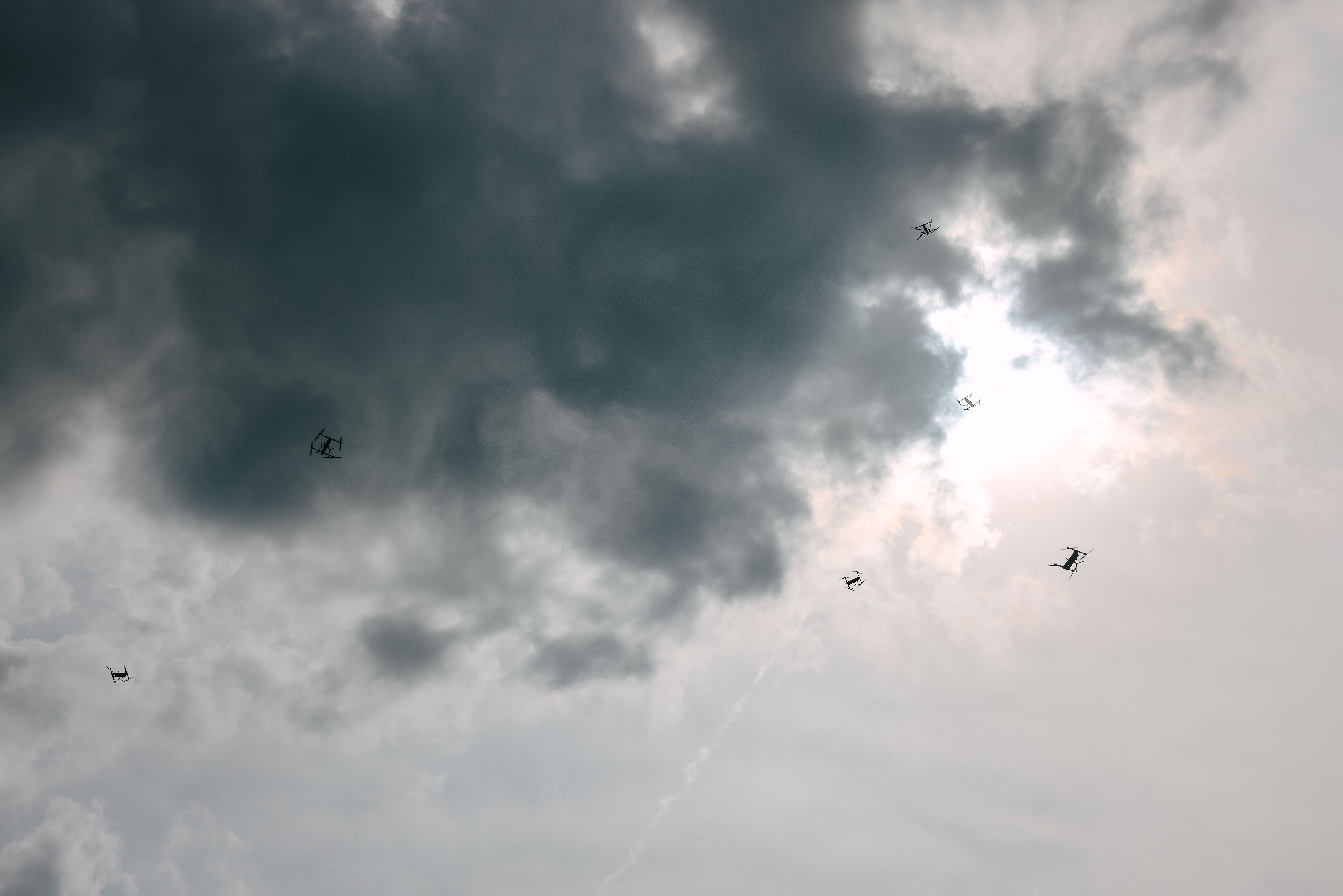 Six small drones fly in an overcast, grey sky.