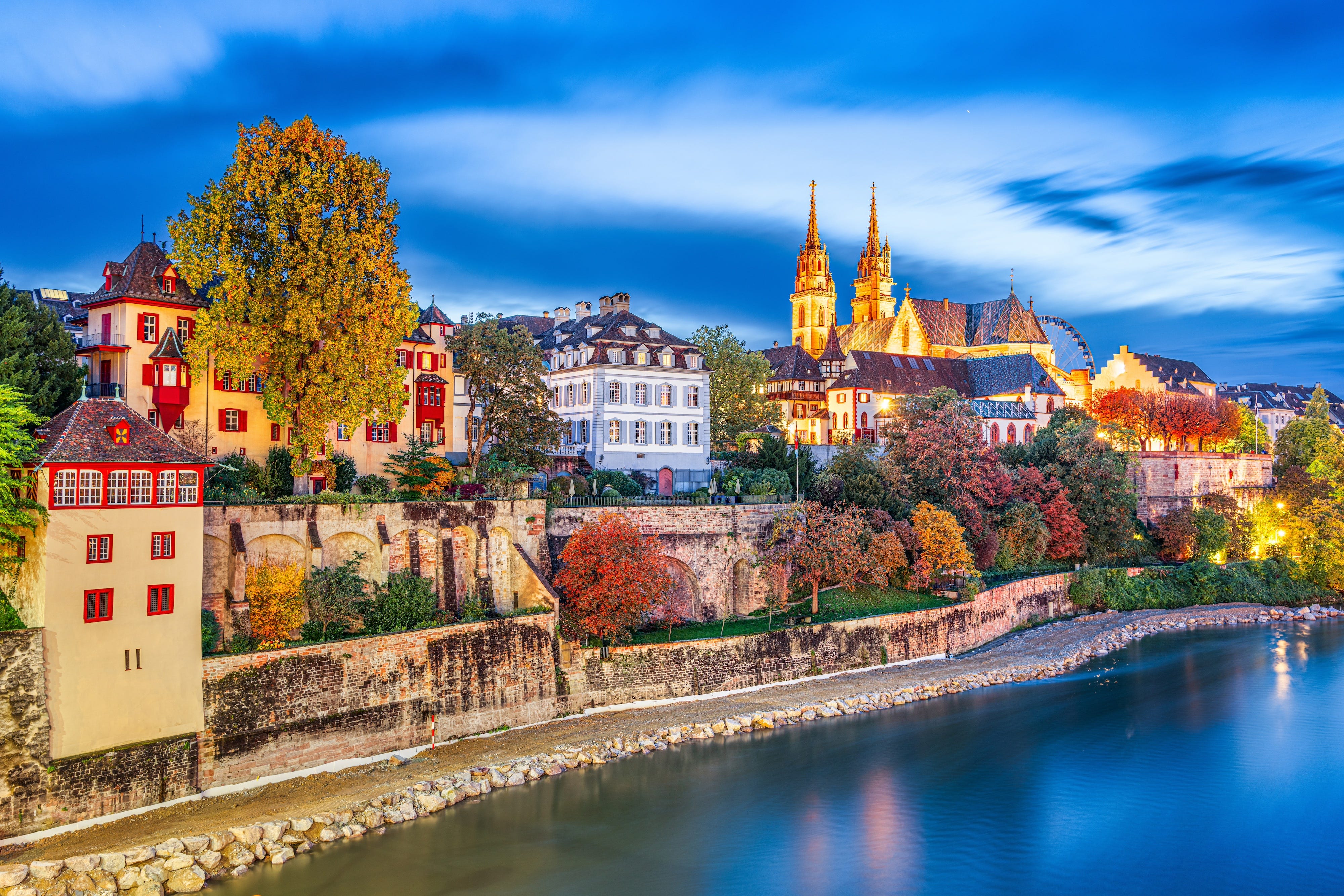 Buildings in Basel, Switzerland, along the Rhine River. The trees are different shades of autumnal colors.