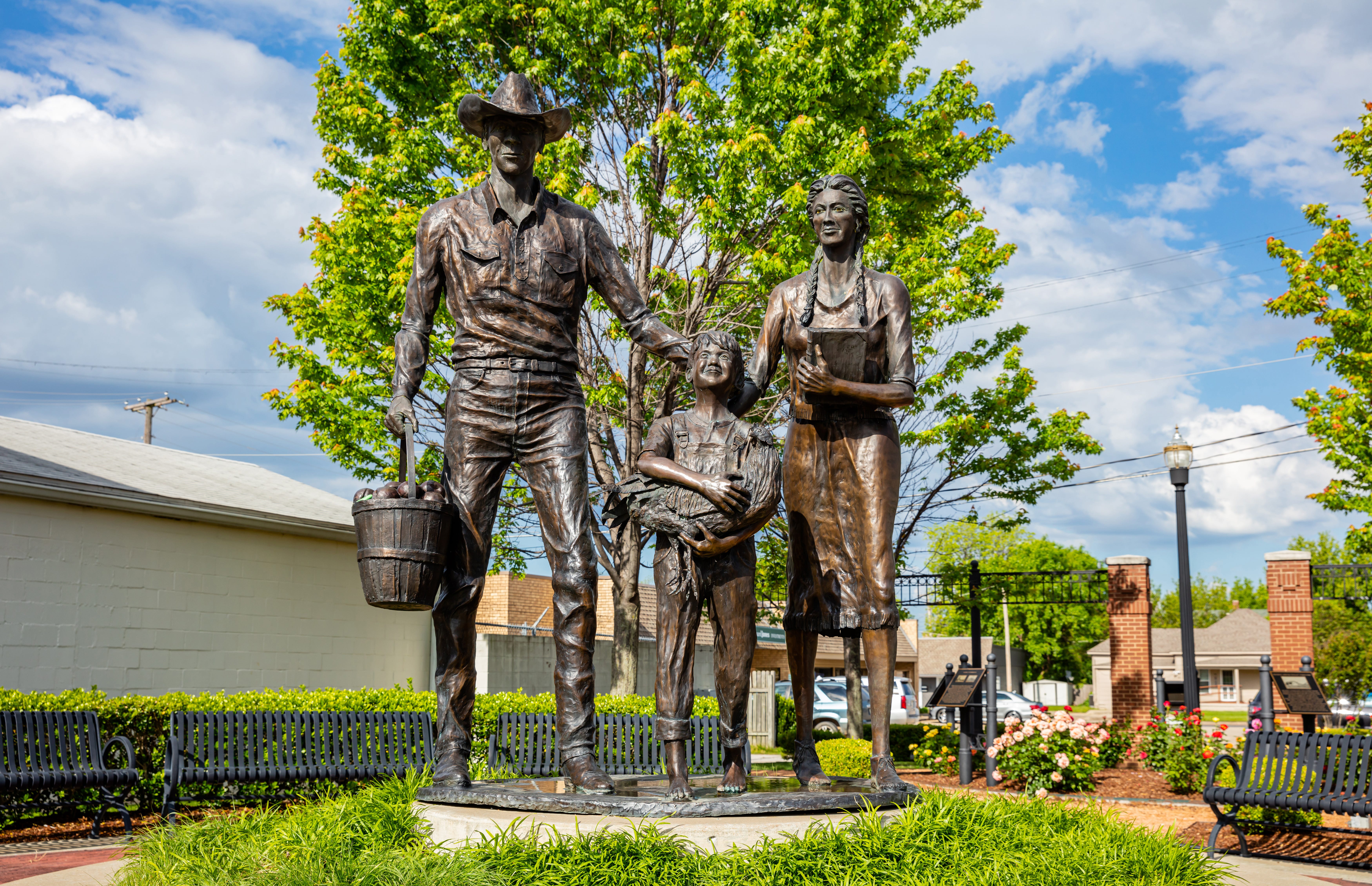 A bronze station with a man, woman, and child holding a basket, rooster, and book