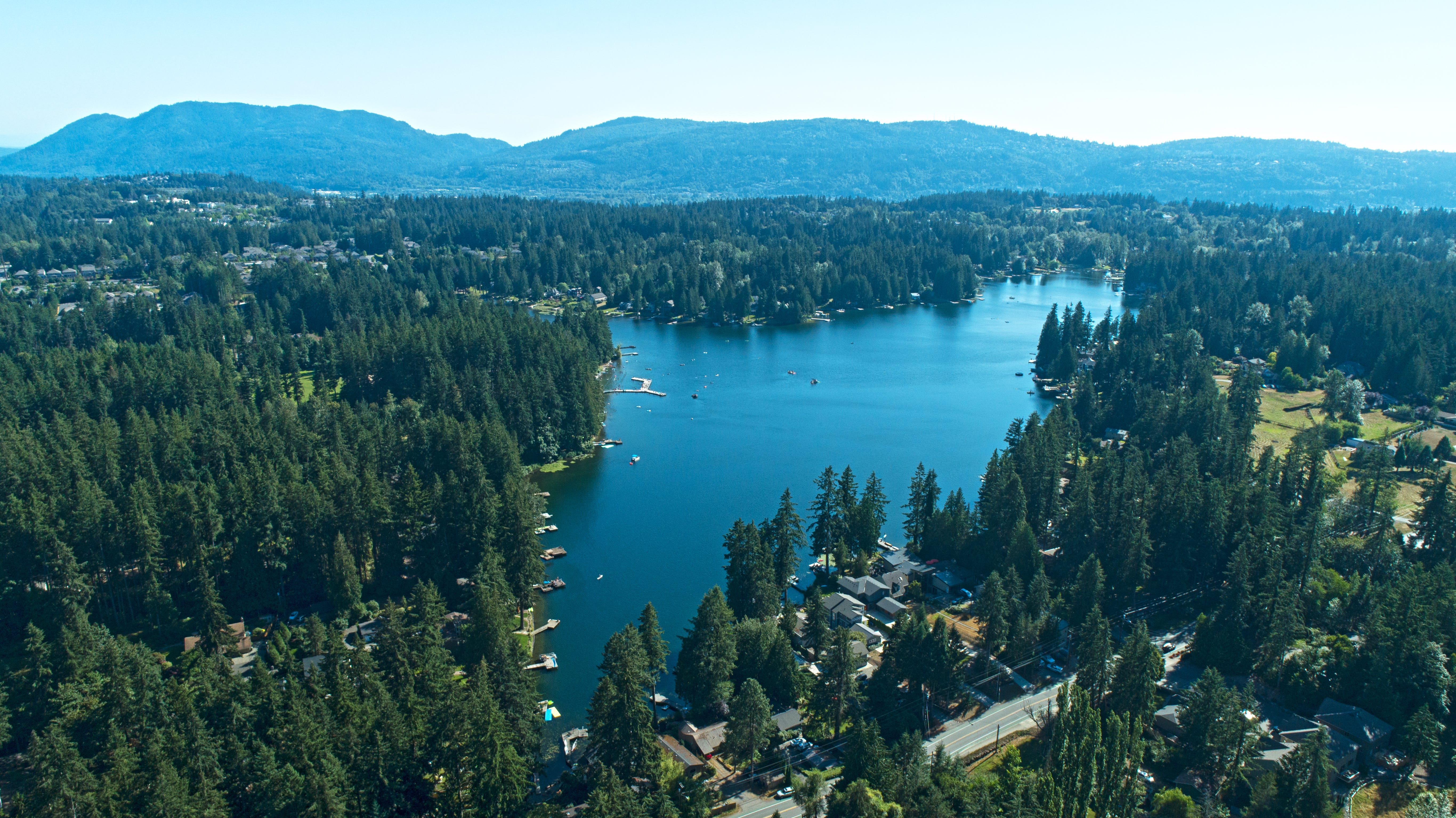 A lake surrounded by trees with houses on the waterfront and hills in the background