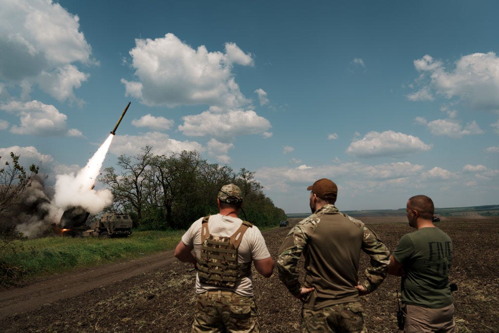 Three Ukrainian troops watch as a rocket is launched in front of them.