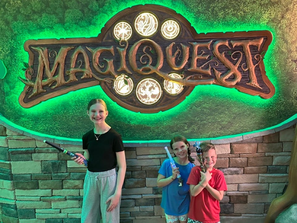 Kids standing in front of lit-up MagiQuest sign at Great Wolf Lodge holding wands