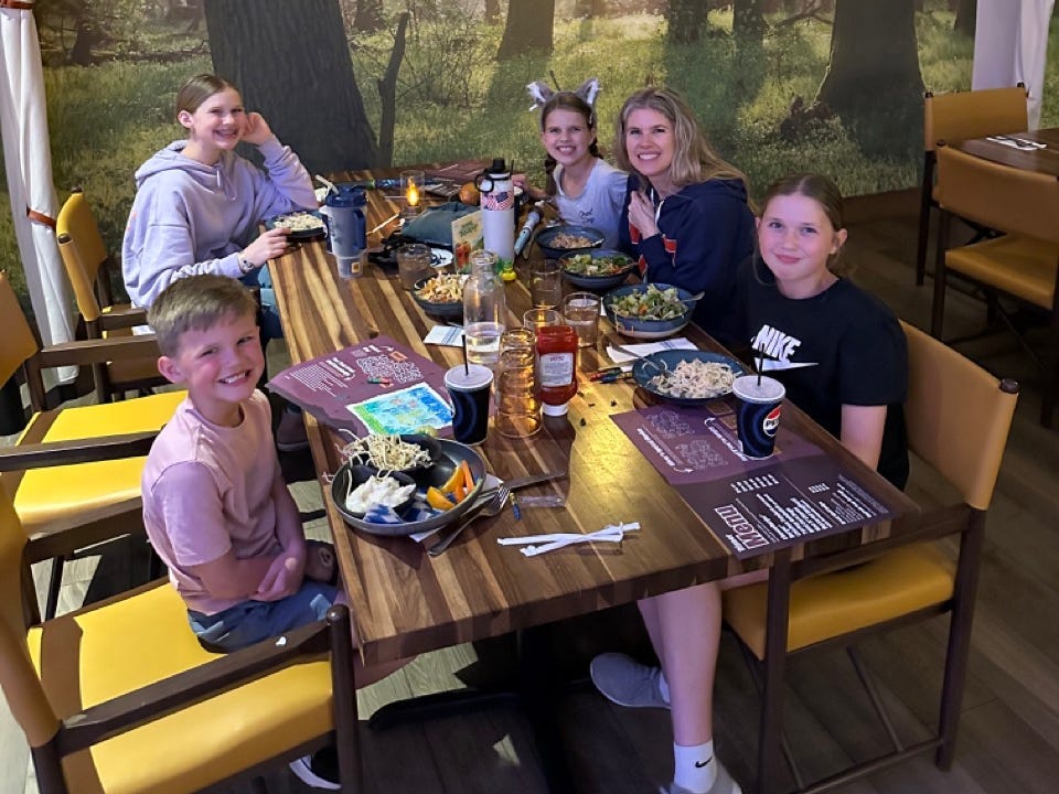 Family sitting at wood table in front of tree-covered wallpaper at GReat Wolf Lodge