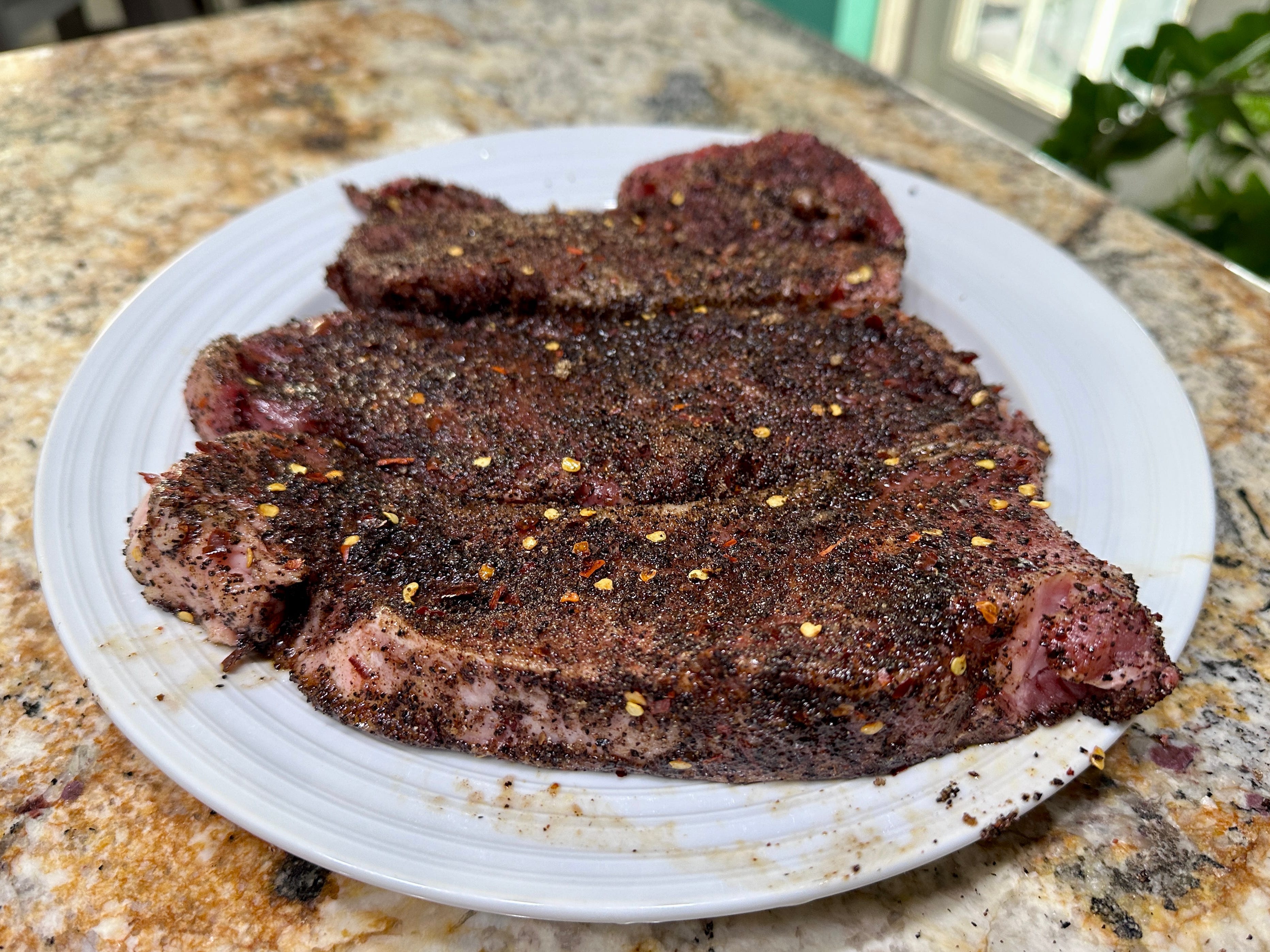 Three steaks covered in spices on a white plate.