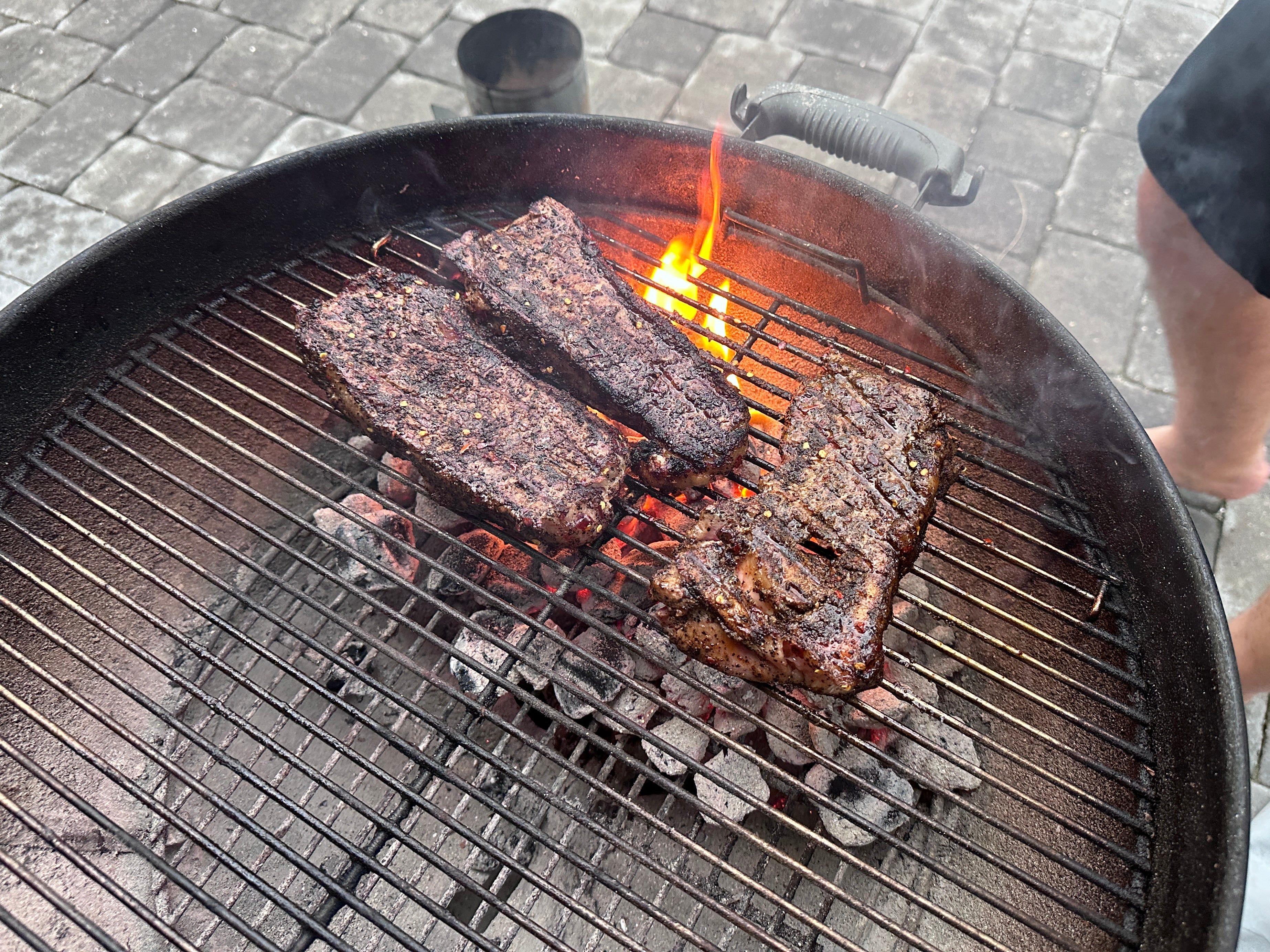 Three steaks cooking on a charcoal grill, with the charcoals only on one side of the grill.
