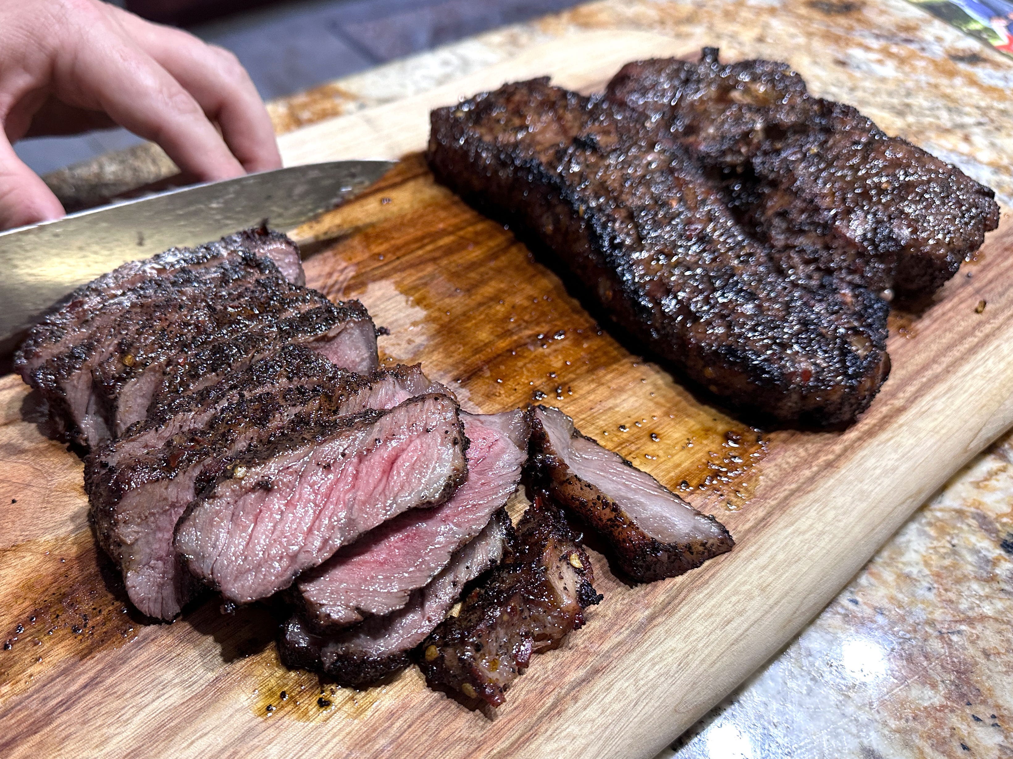 One piece of steak being sliced on a cutting board, with two full pieces resting behind it.