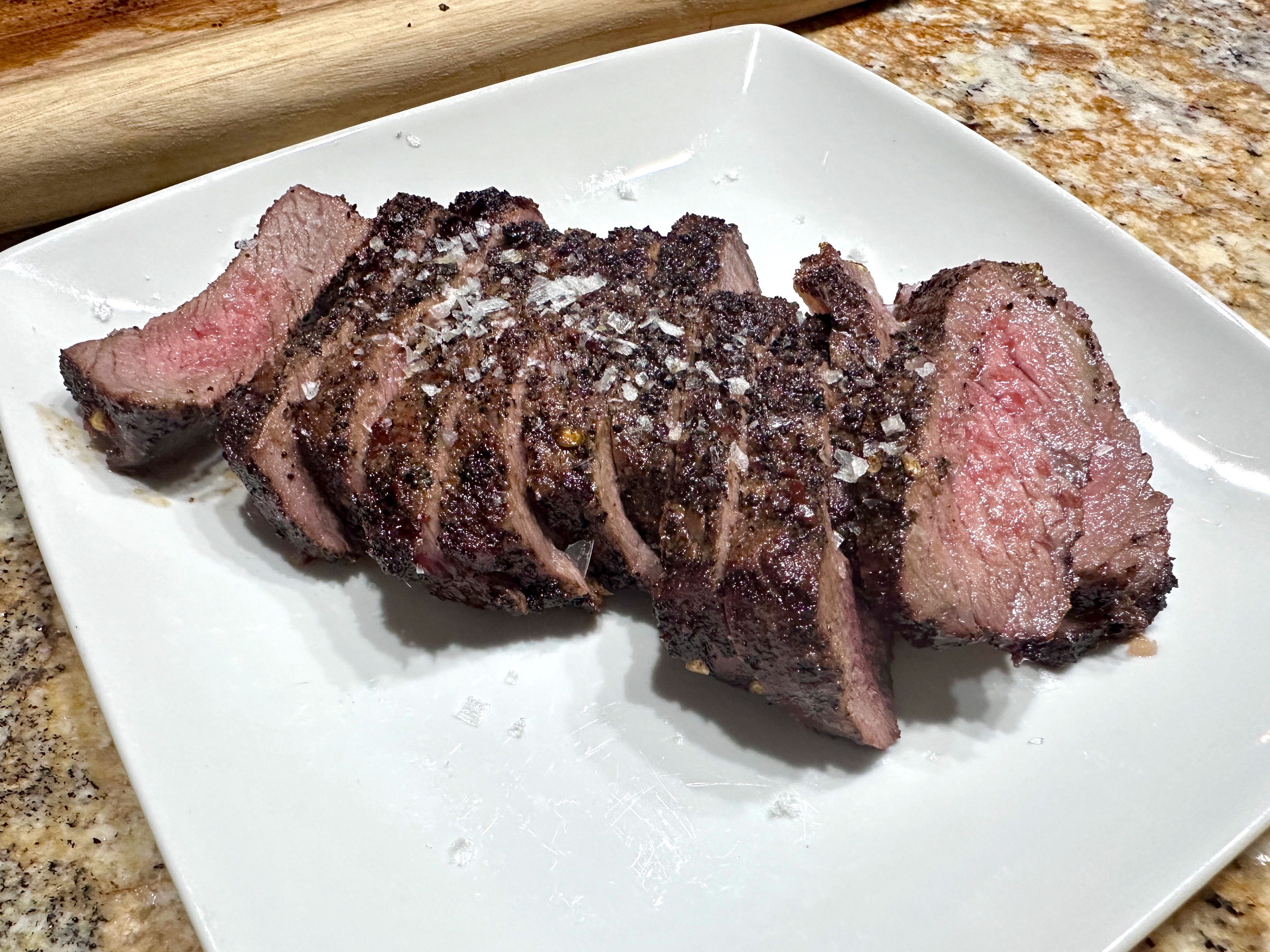Sliced steak topped with flakes of salt on a white plate.