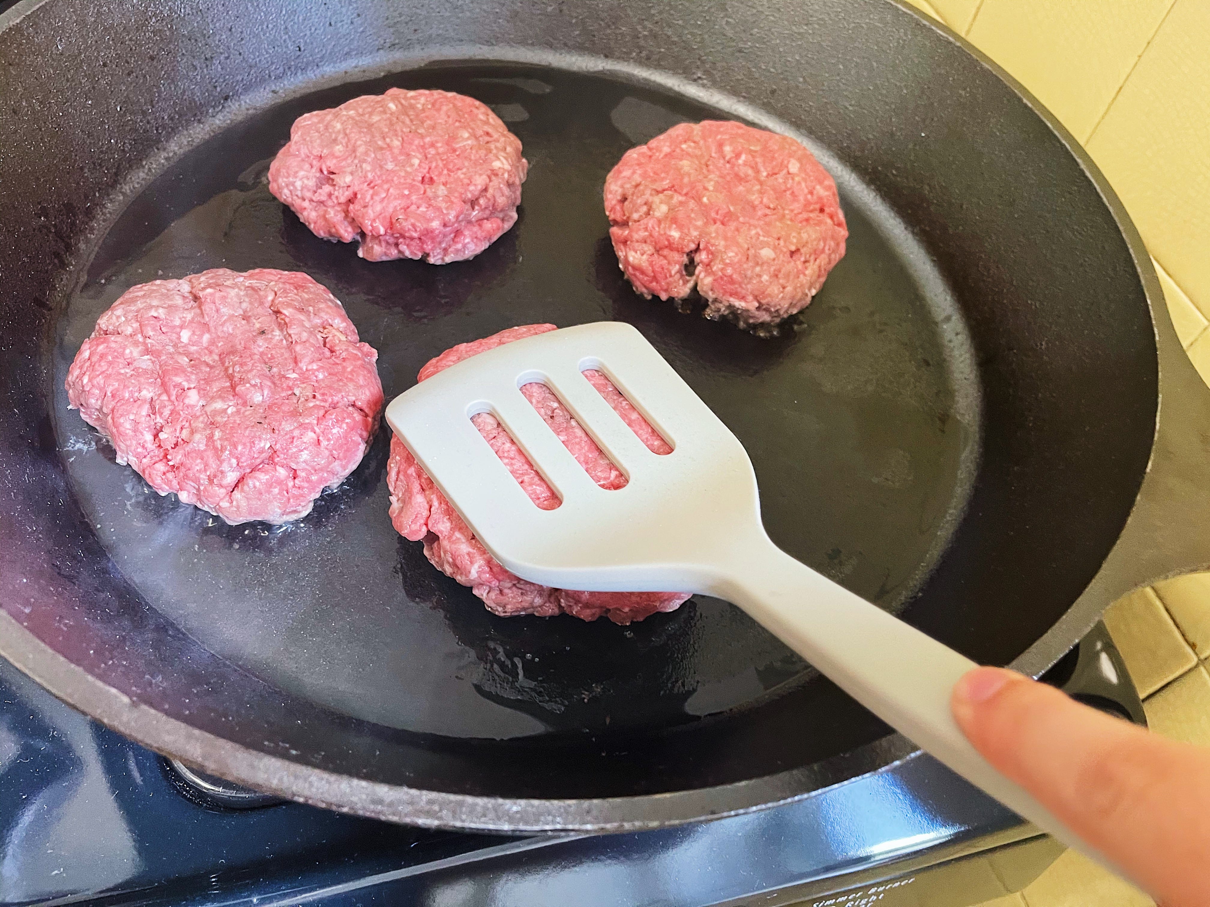 burger patties in a cast iron skillet with a spatula