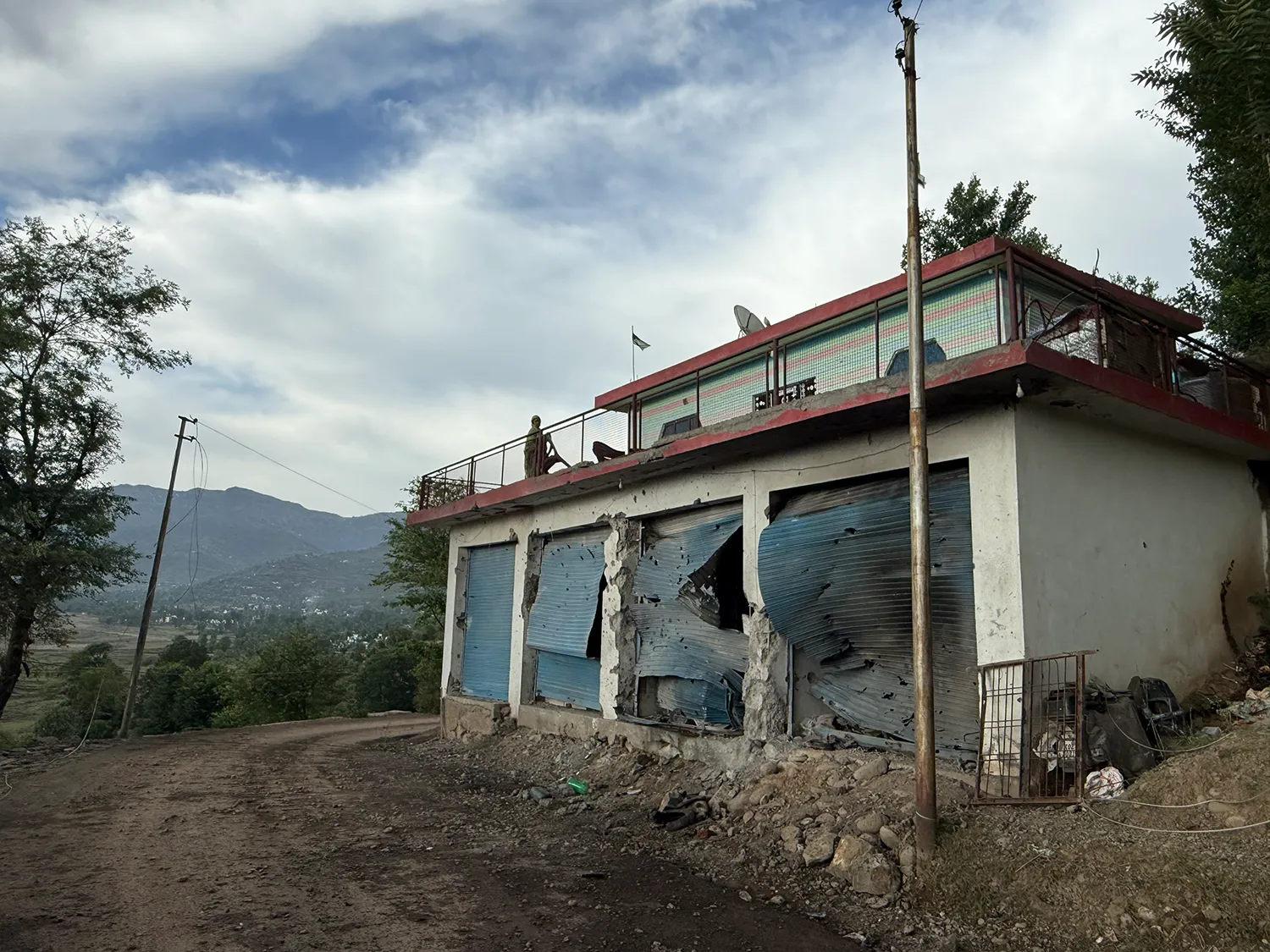 A dirt road passes a building with four damaged corragated doors.