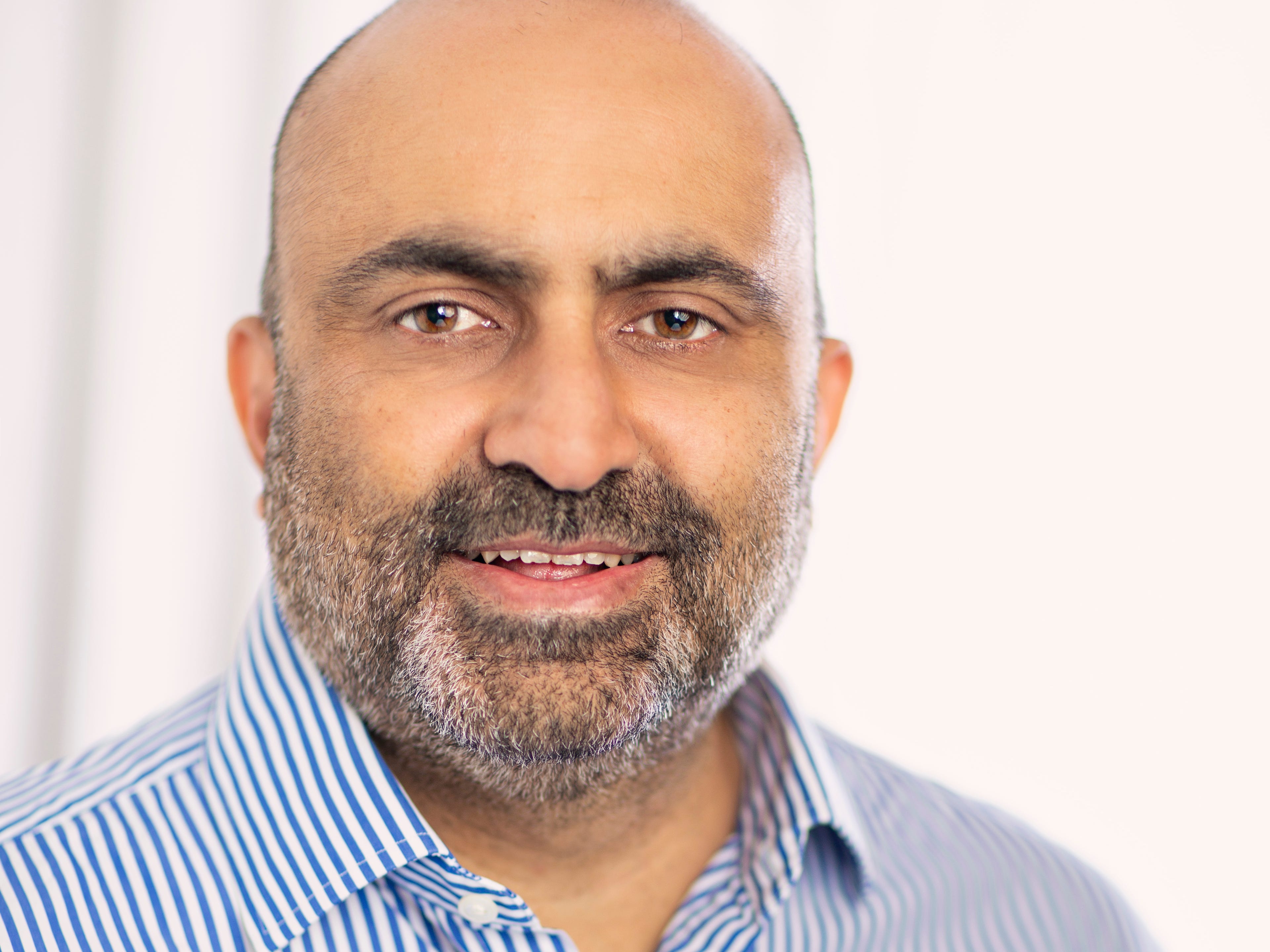 Hitendra Merchant headshot, wearing a blue and white striped shirt.