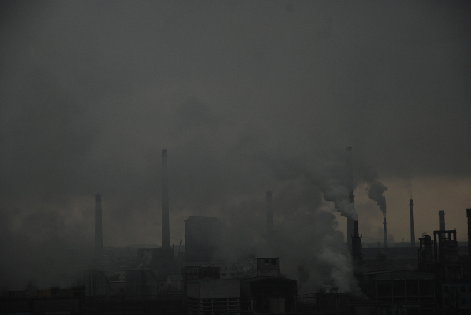 Smokestacks of a factory are seen obscured by a cloud of pollution.
