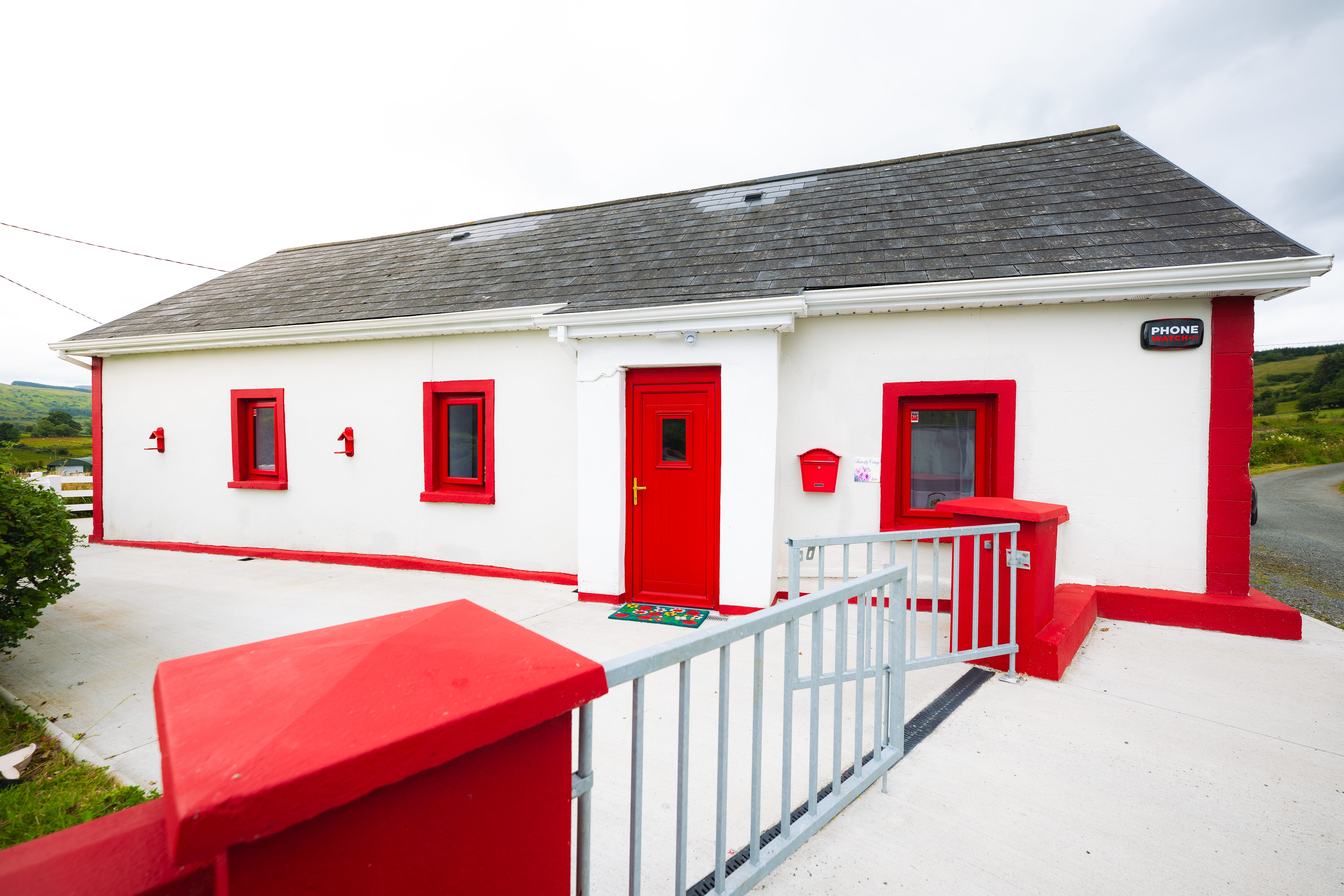 A white single-story house with red doors and red window shutters called Butterfly Cottage