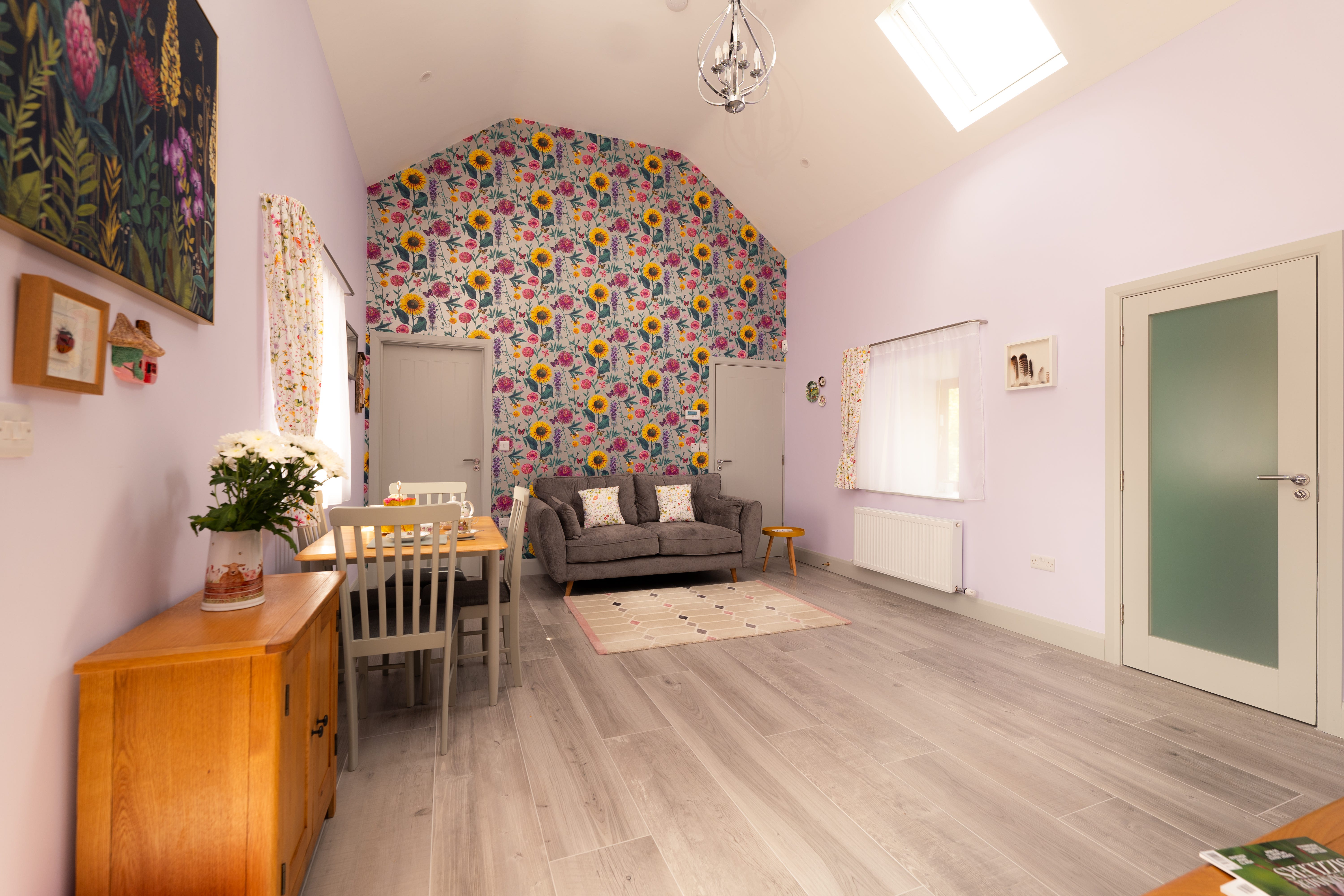 A living/dining room with a vaulted ceiling, colorful wallpaper, a couch, and a dining table