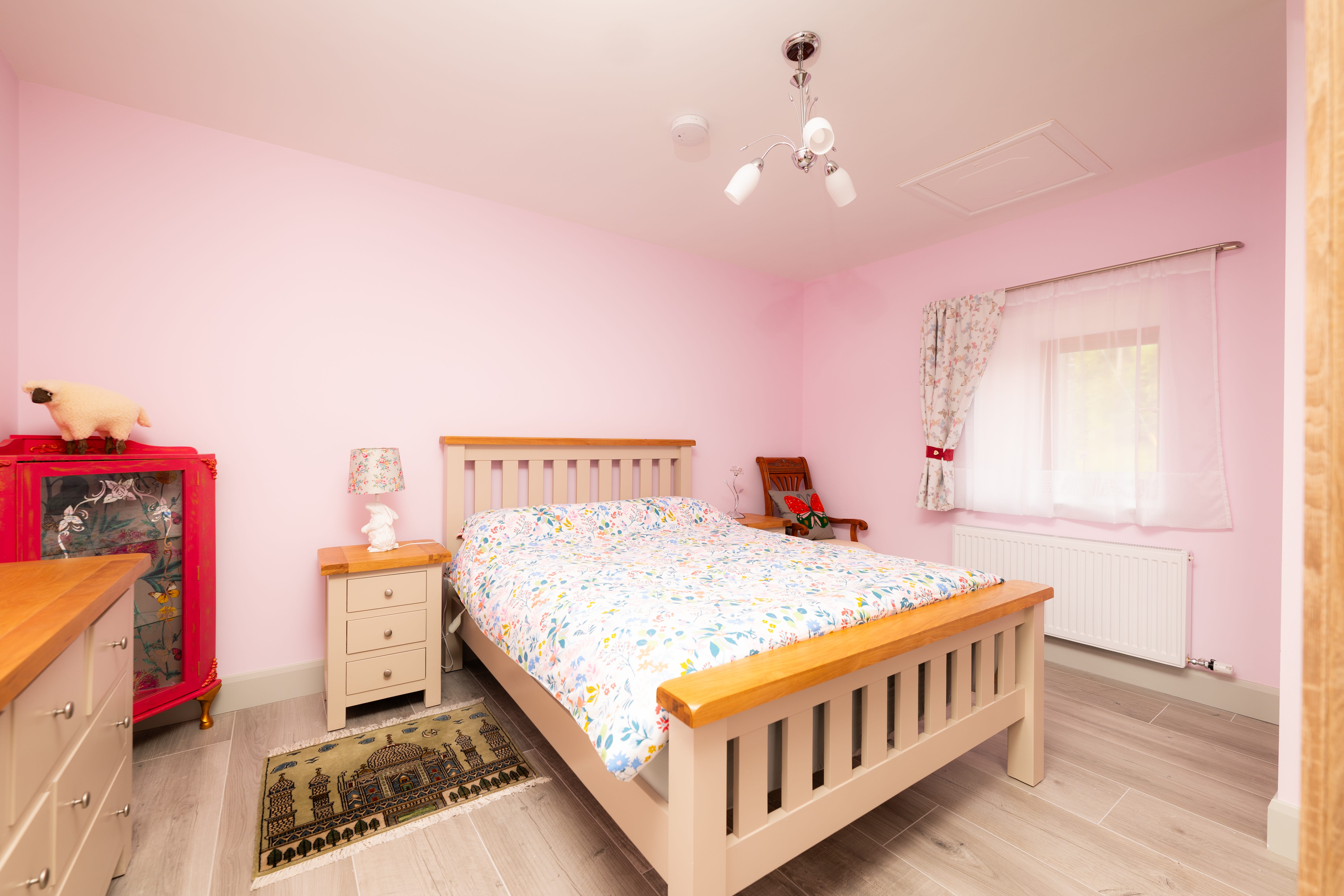 A bedroom with pink walls and a bed with a flowered bedspread, with a nightstand to one side