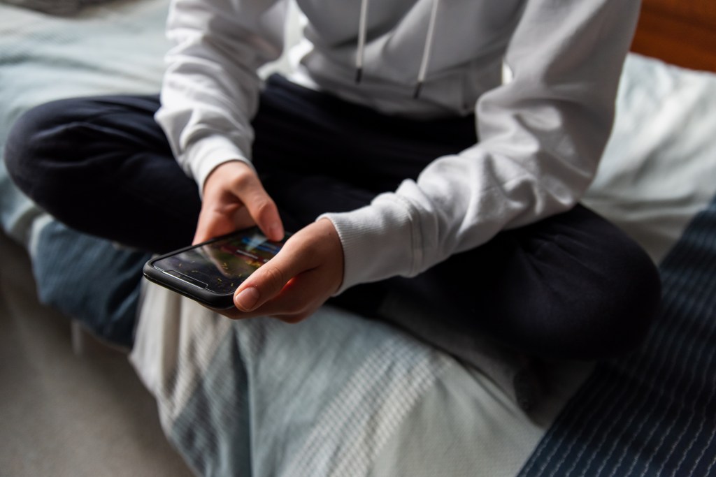 Close up of a teen boy's hands in a white sweater texting on a mobile phone
