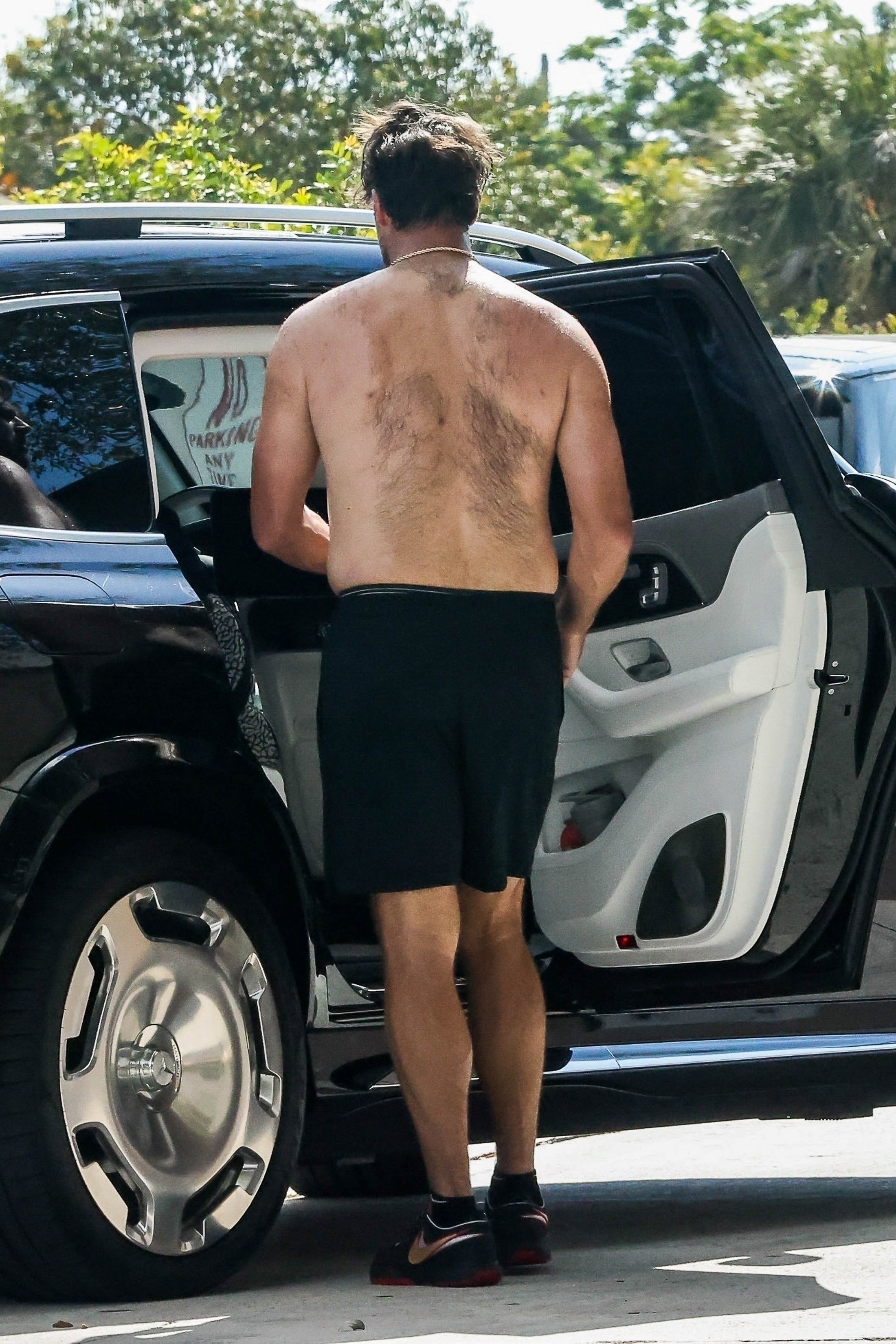 Shirtless Travis Kelce outside a black vehicle. 
