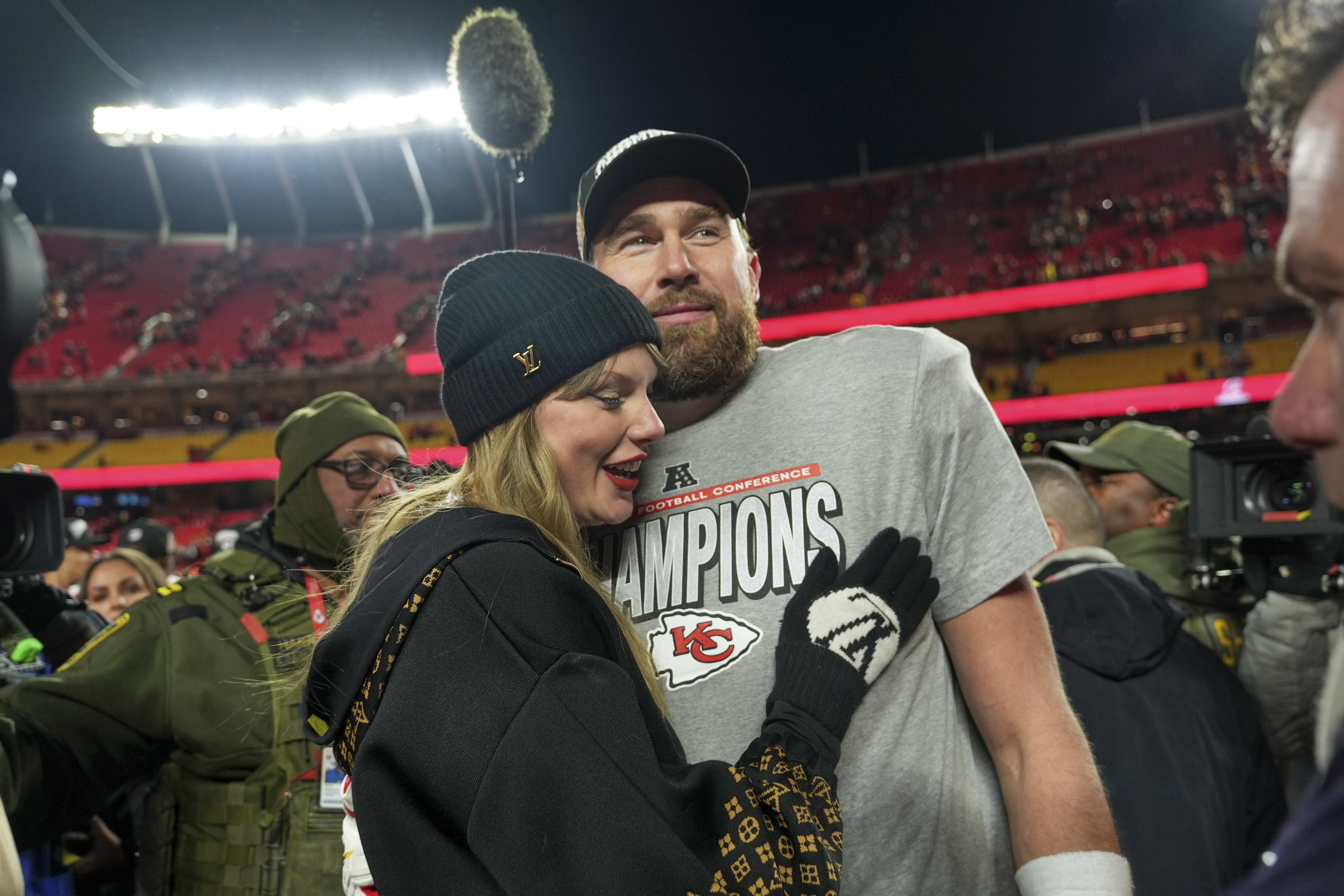 Travis Kelce and Taylor Swift hug on a football field. 