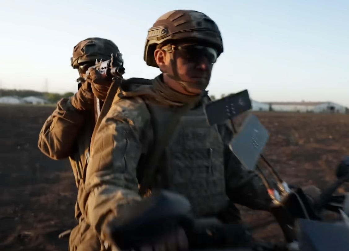A Ukrainian soldier points their AK-74U assault rifle over the shoulder of a comrade driving a motorbike.