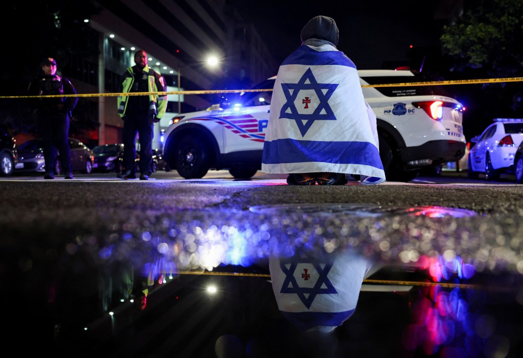 A bystander wears an Israeli flag while a police officer looks on near the scene of the shooting.