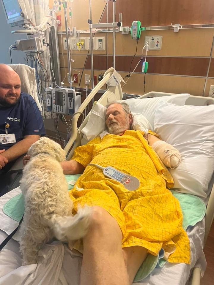 Paul Cline, whose arm was torn off holding on to his wife during a tornado, is comforted by his dog Sadie in a hospital bed.