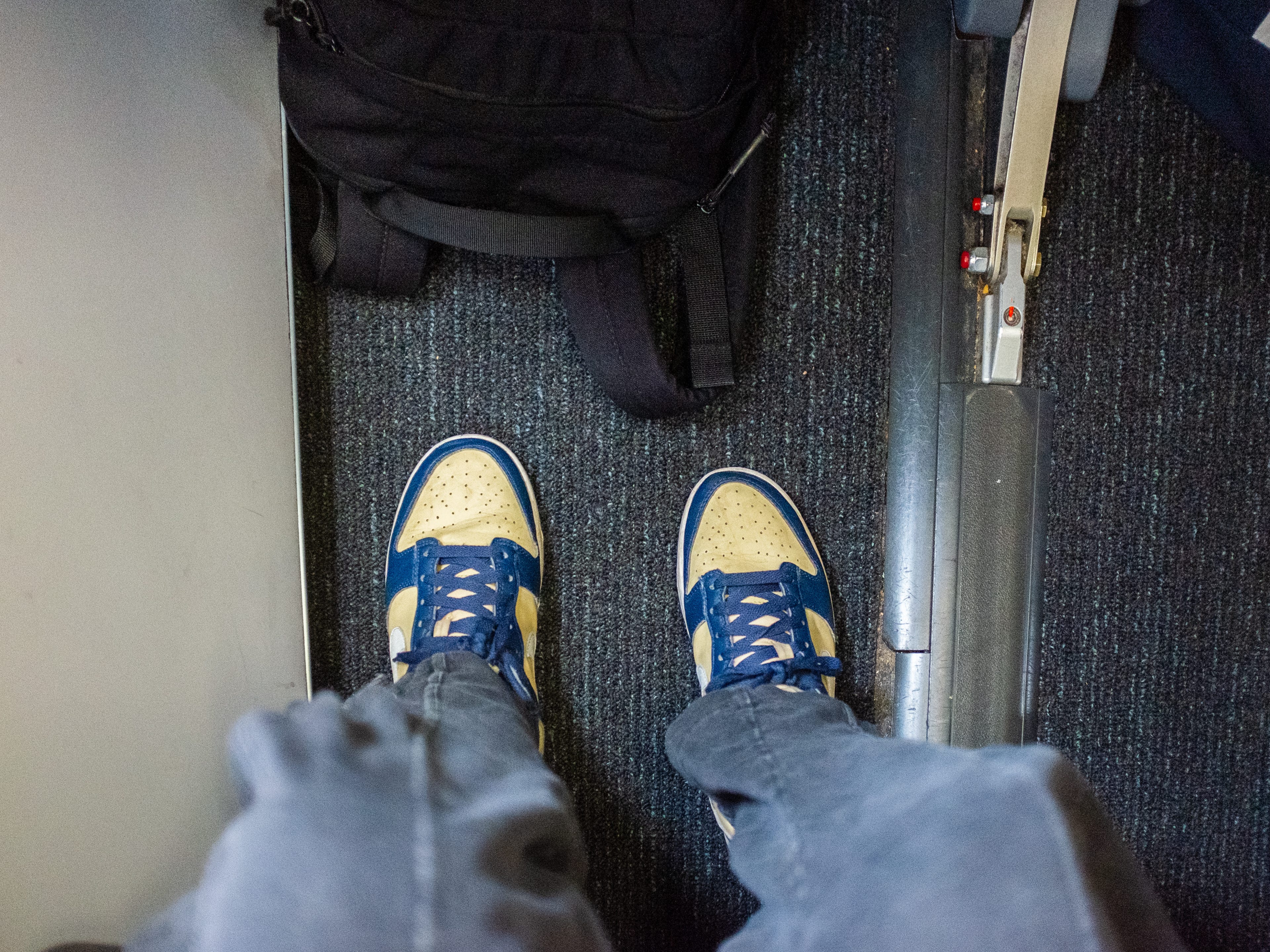 An aerial view of the authors leg room wearing sweats and sneakers with a backpack under the seat in front