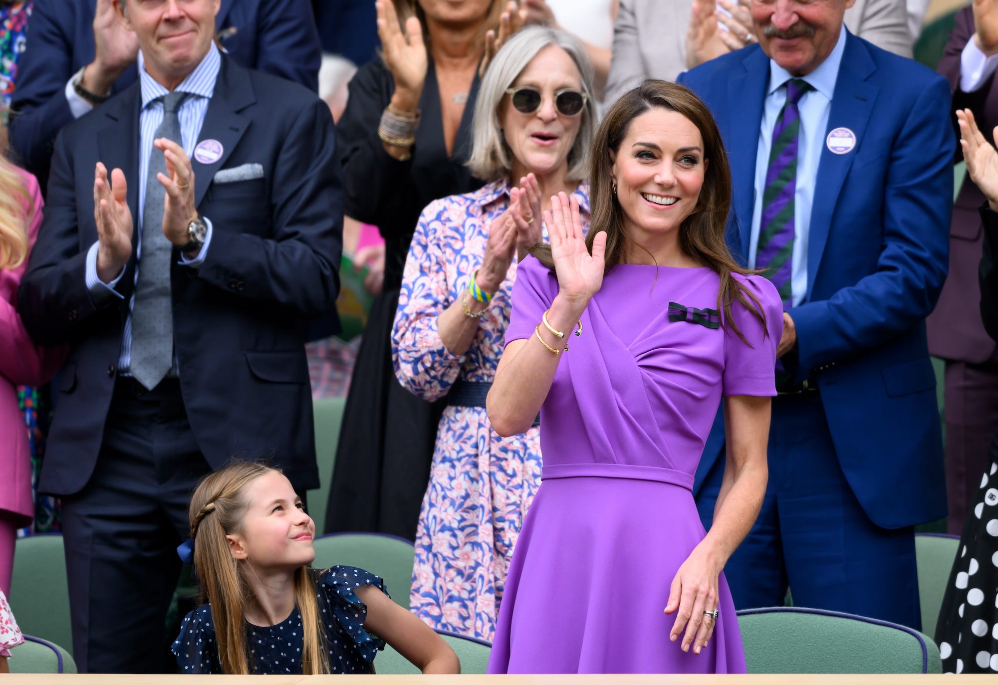 Princess Charlotte, dressed in a blue polka-dot dress, and Kate Middleton, dressed in a purple dress, sit in a crowd at Wimbledon.