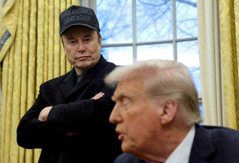 Elon Musk (left) in a black cap listens to President Donald Trump speak in the Oval Office of the White House.