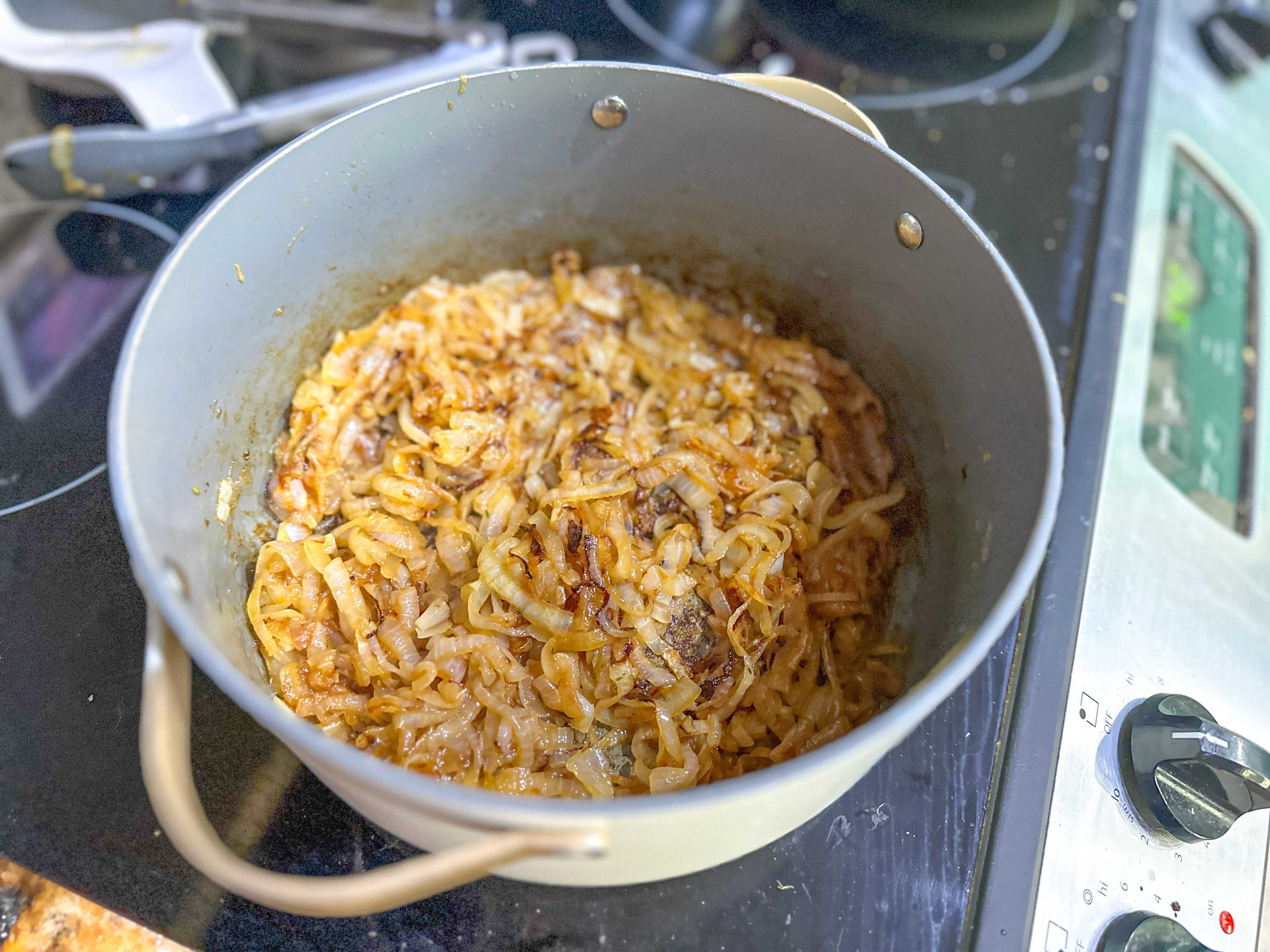 A large gray pot holding caramelized onions cooking on a stove