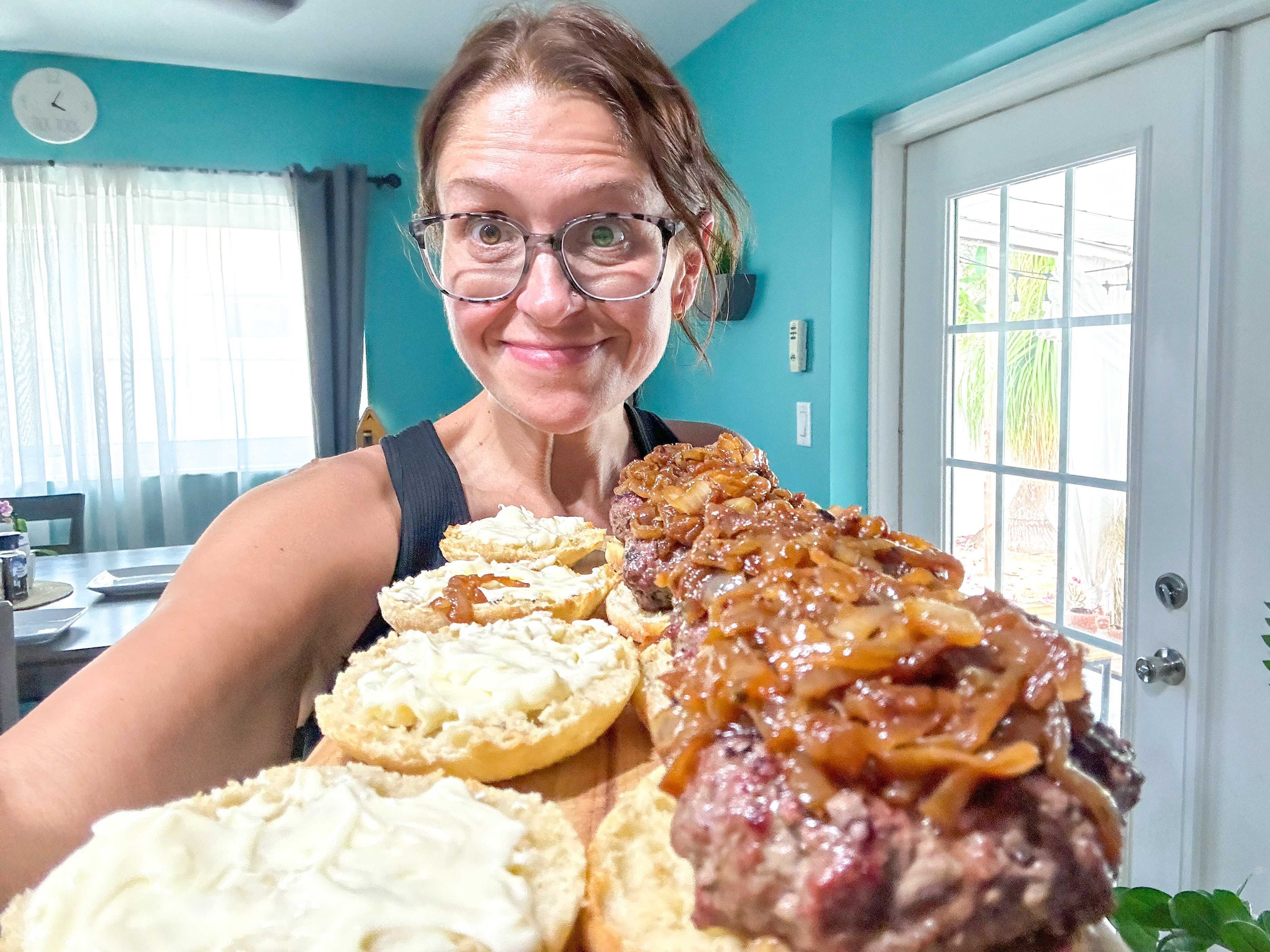 The writer holds wooden board with plated burgers on English muffins topped with caramelized onions