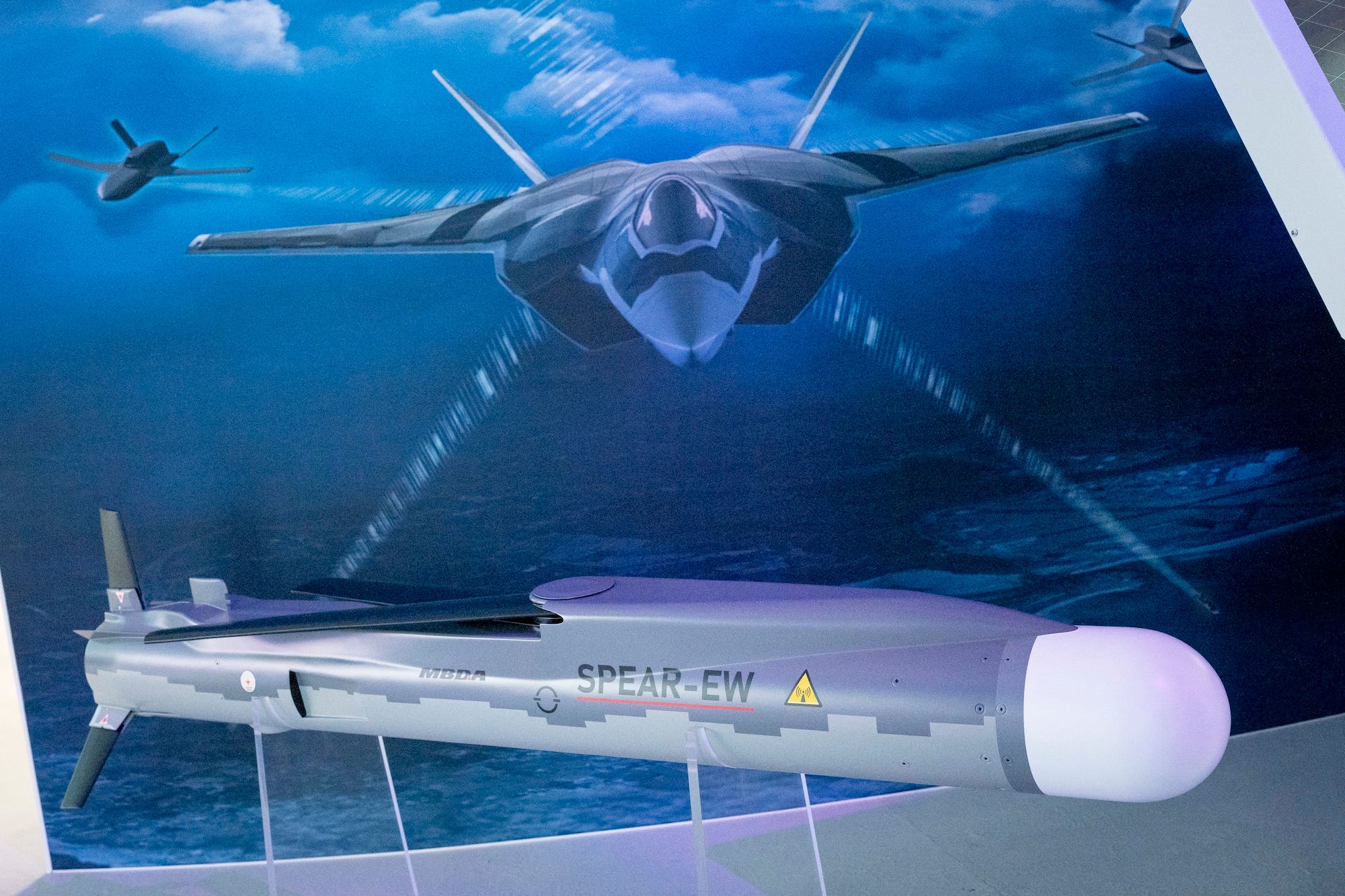 A grey missile on display against a blue backdrop that has a picture of an F-35 fighter jet on it