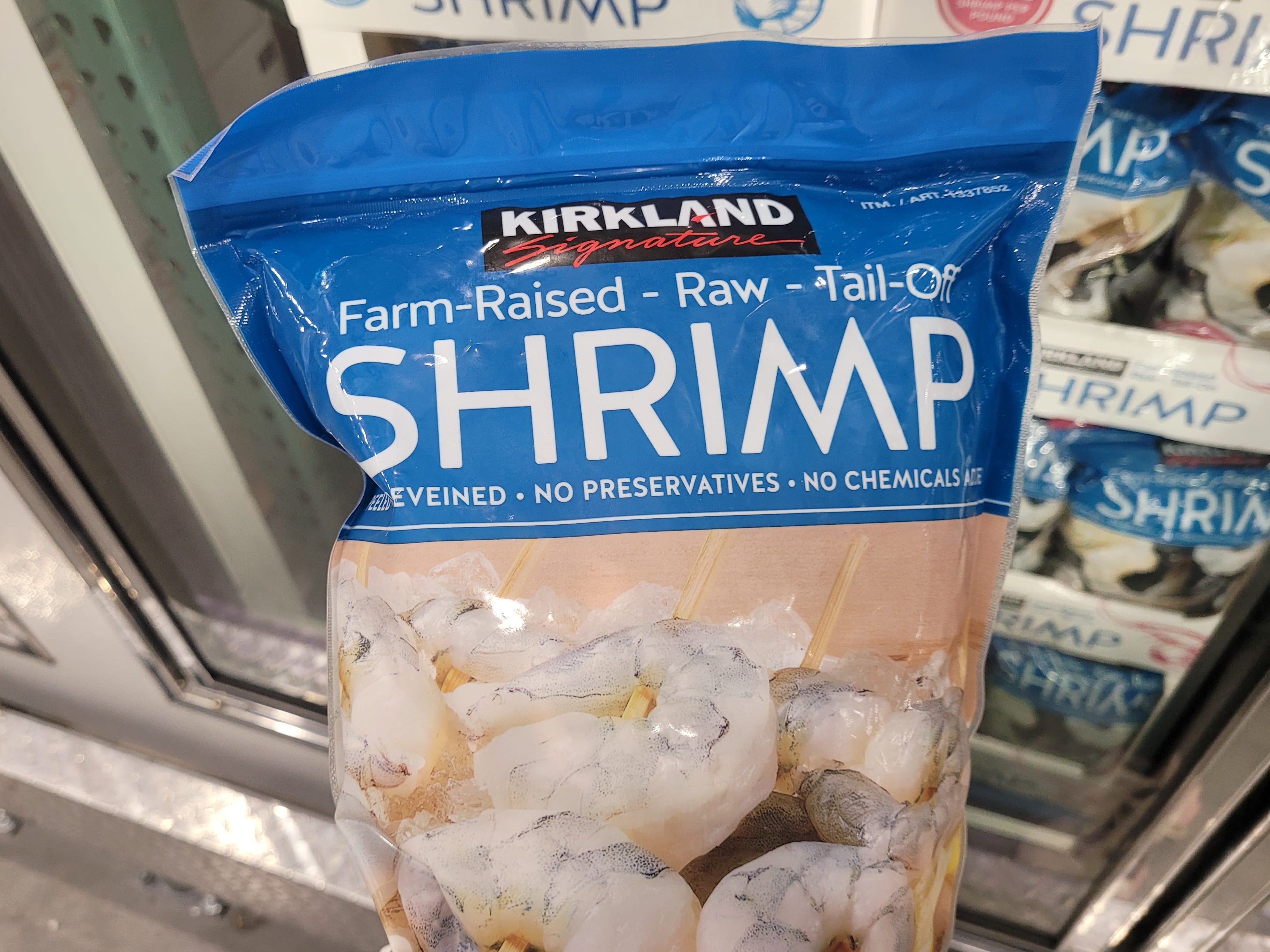 A bag of Kirkland frozen shrimp held in front of a freezer case.