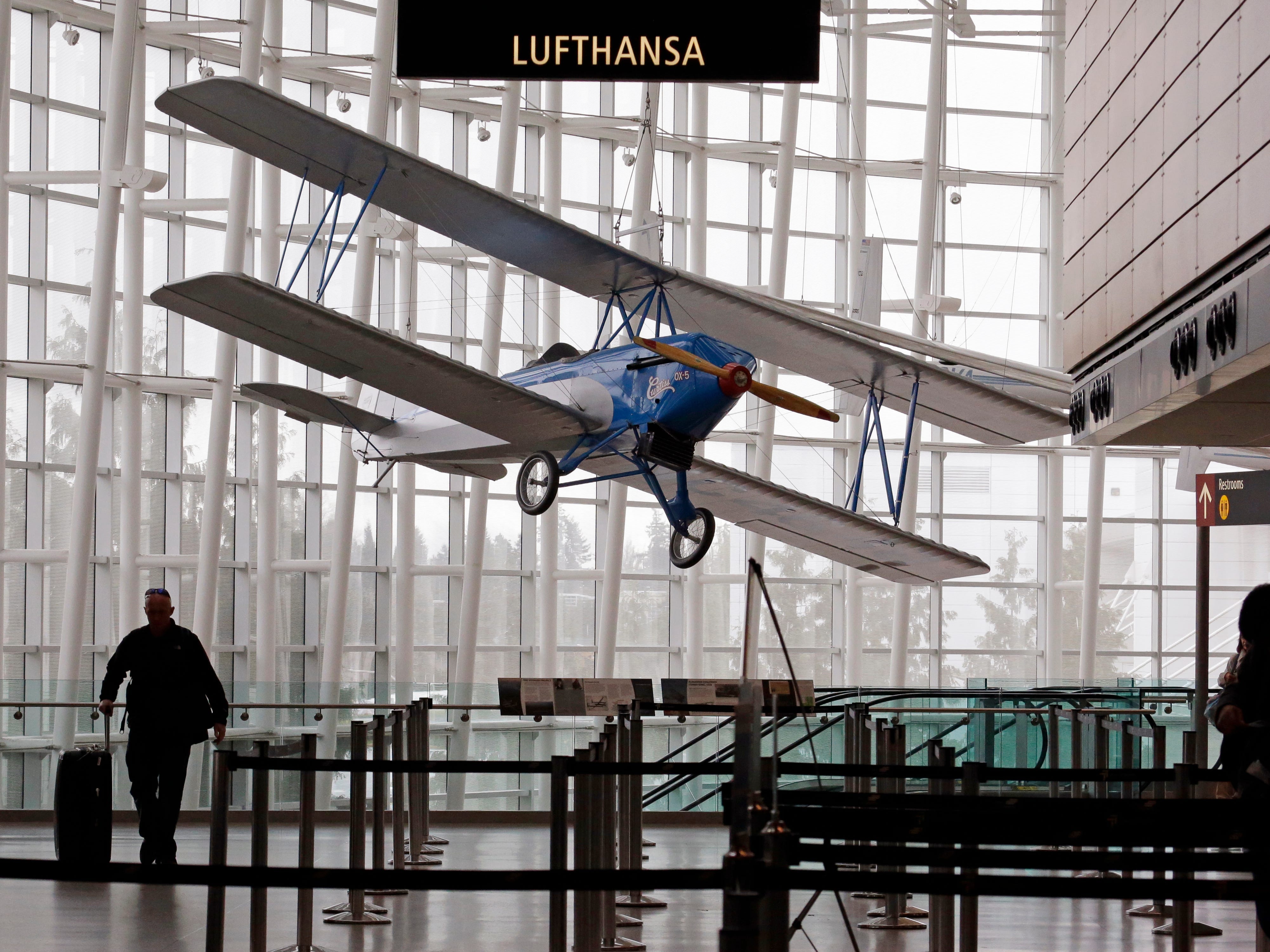 An airline traveler walks in view of a 1926 Alexander Eaglerock Combo-Wing airplane displayed at Seattle-Tacoma International Airport in SeaTac, Wash.